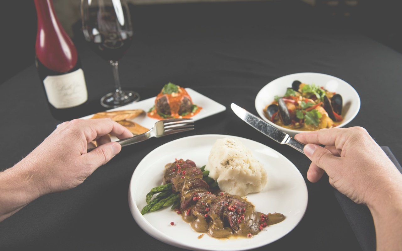 A person is sitting at a table with plates of food and a glass of wine.