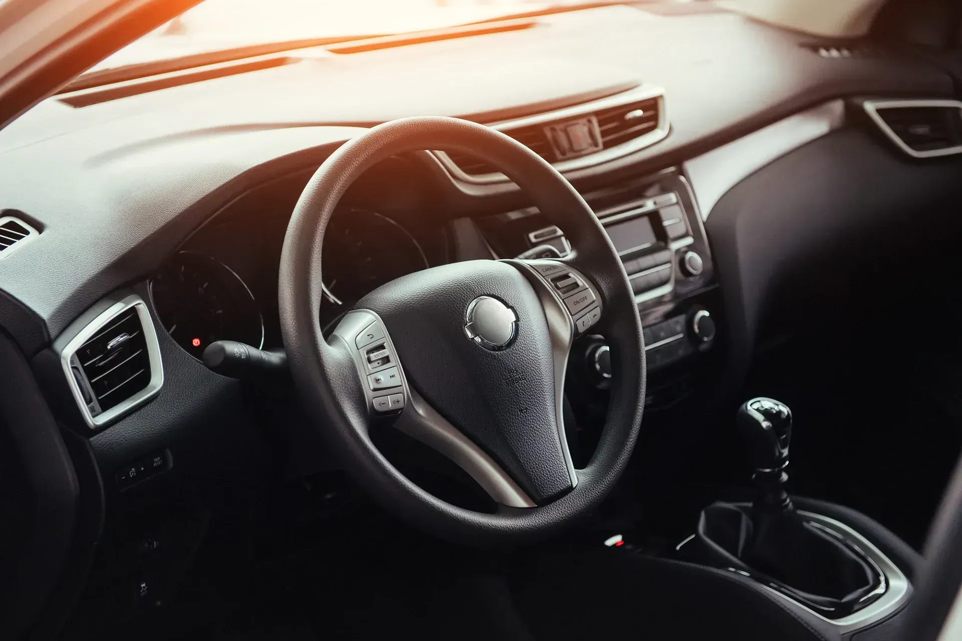 Interior view of a car, showing the steering wheel, dashboard, and gear shift, with a sunlit interior.