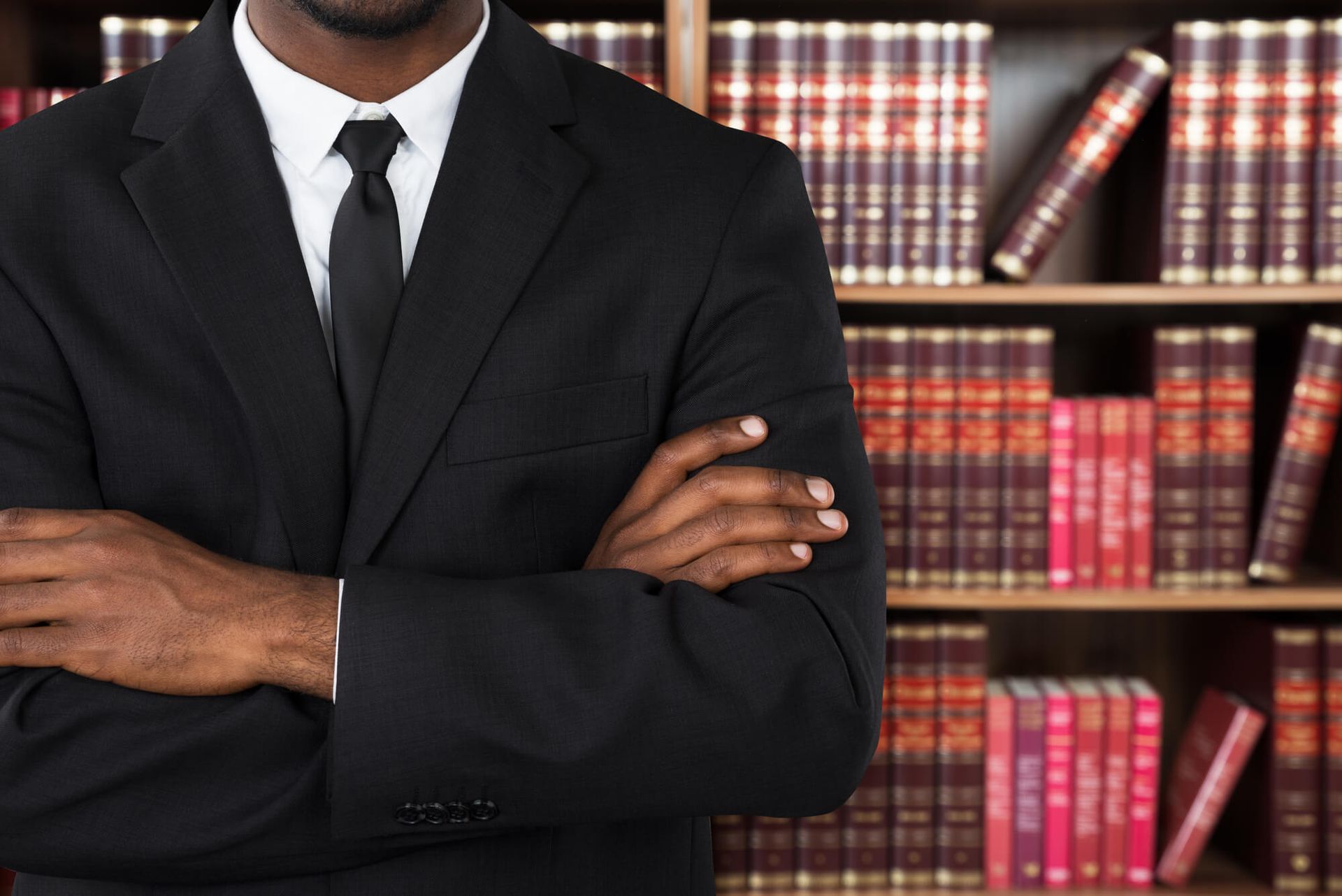 A man in a suit and tie is standing in front of a bookshelf with his arms crossed