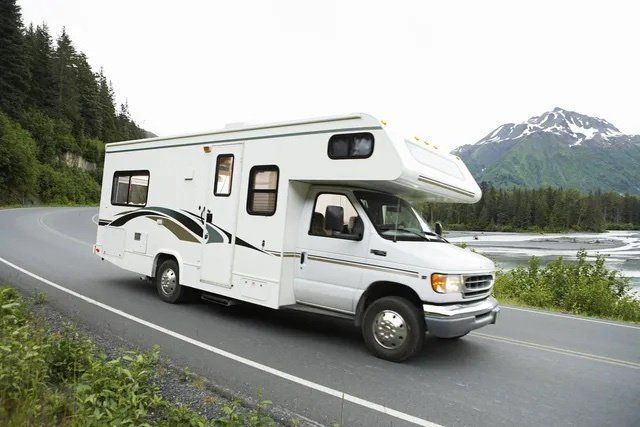 A white rv is driving down a road with mountains in the background.