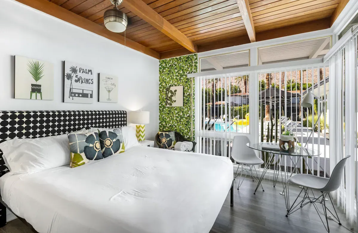 Bright bedroom with white bedding, lime chairs, and a small dining nook under a wood ceiling