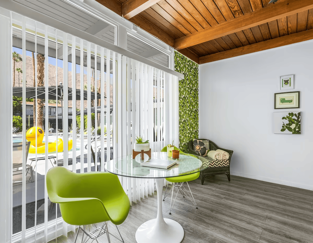 Modern sunroom with green chairs, glass table, vertical blinds, and wood ceiling.