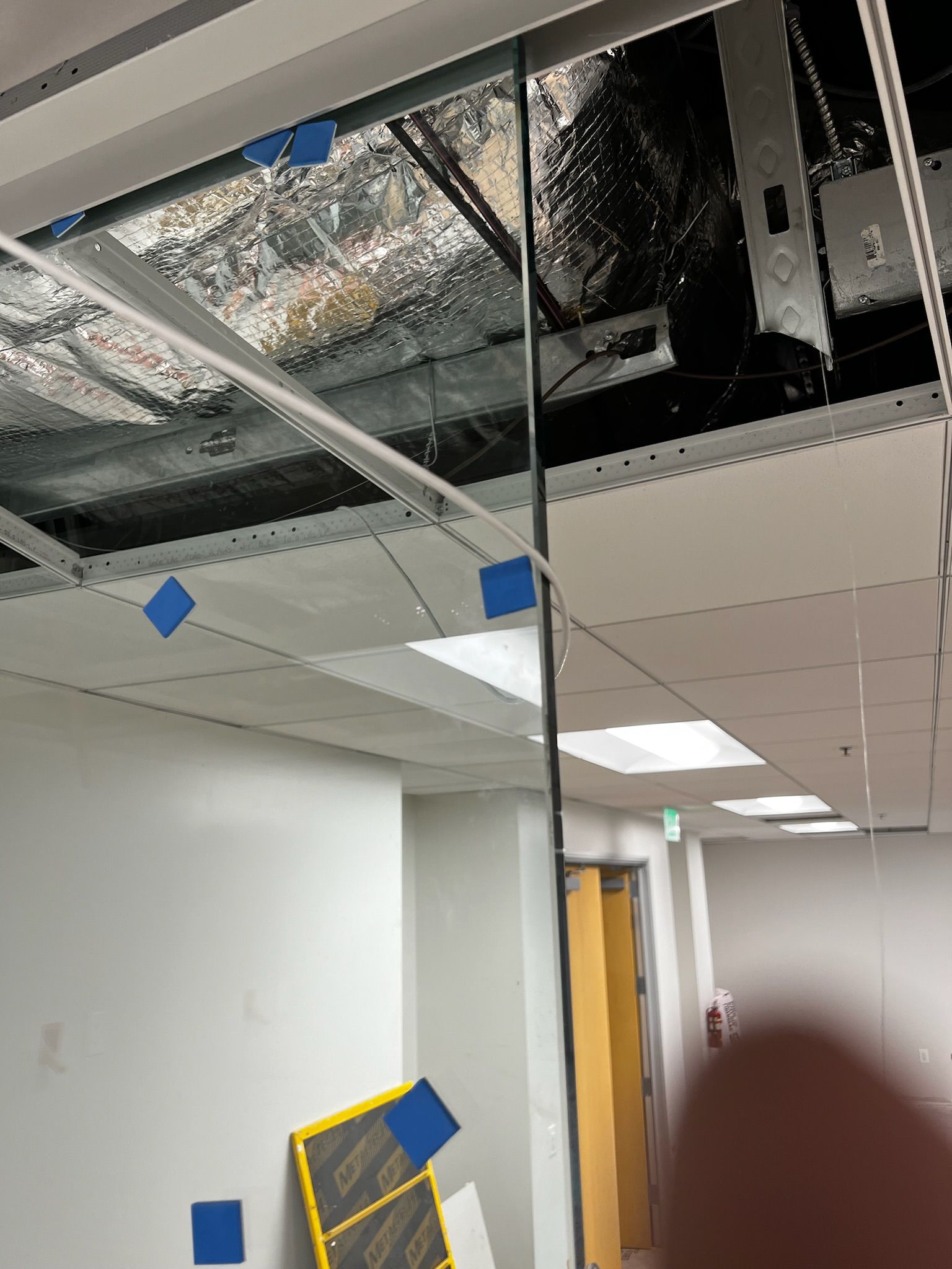 Construction site: exposed ceiling with ductwork, hanging cables, and a partially installed ceiling grid.
