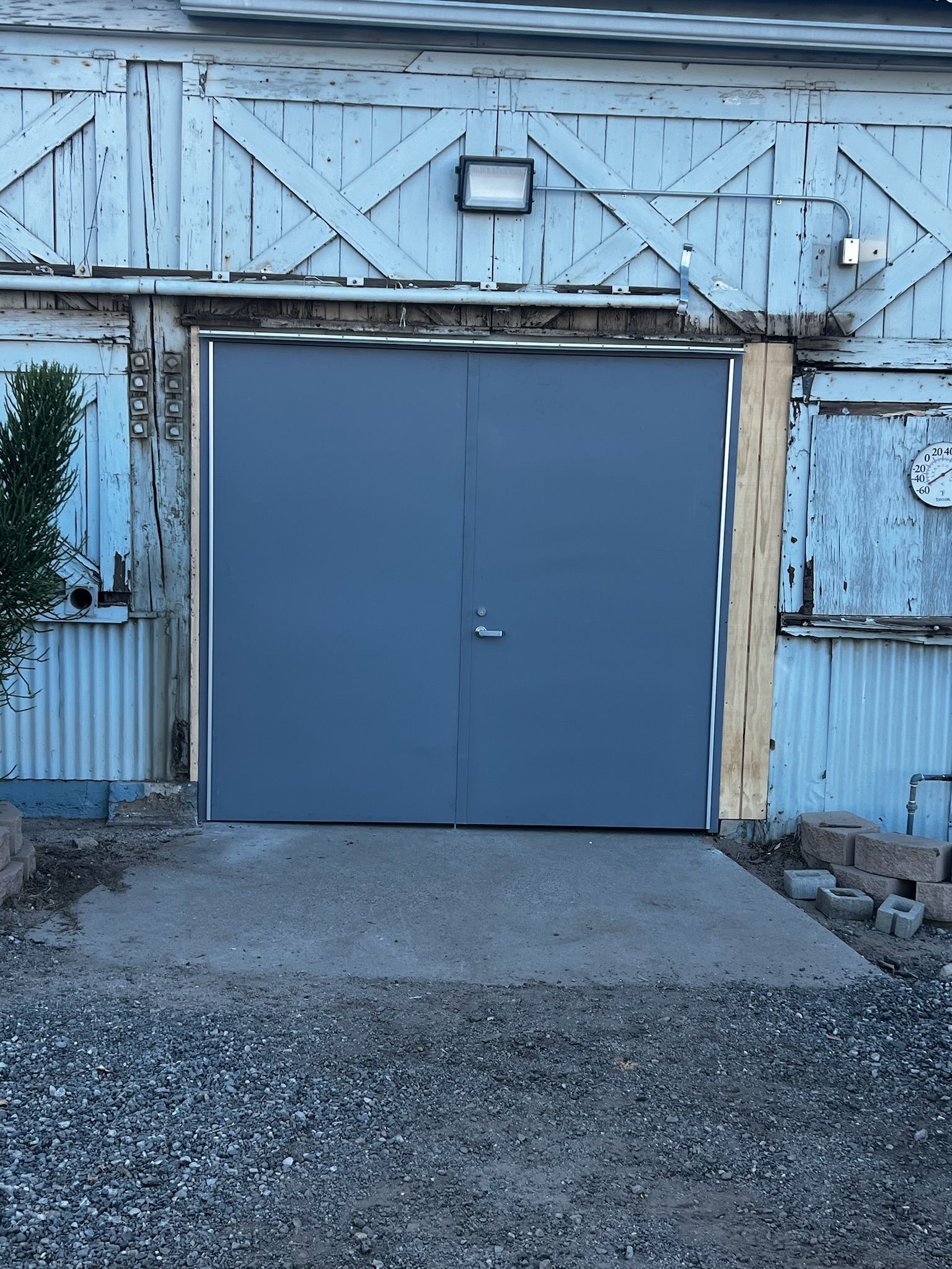 Gray double doors in a weathered, blue building with a concrete ramp leading to them.