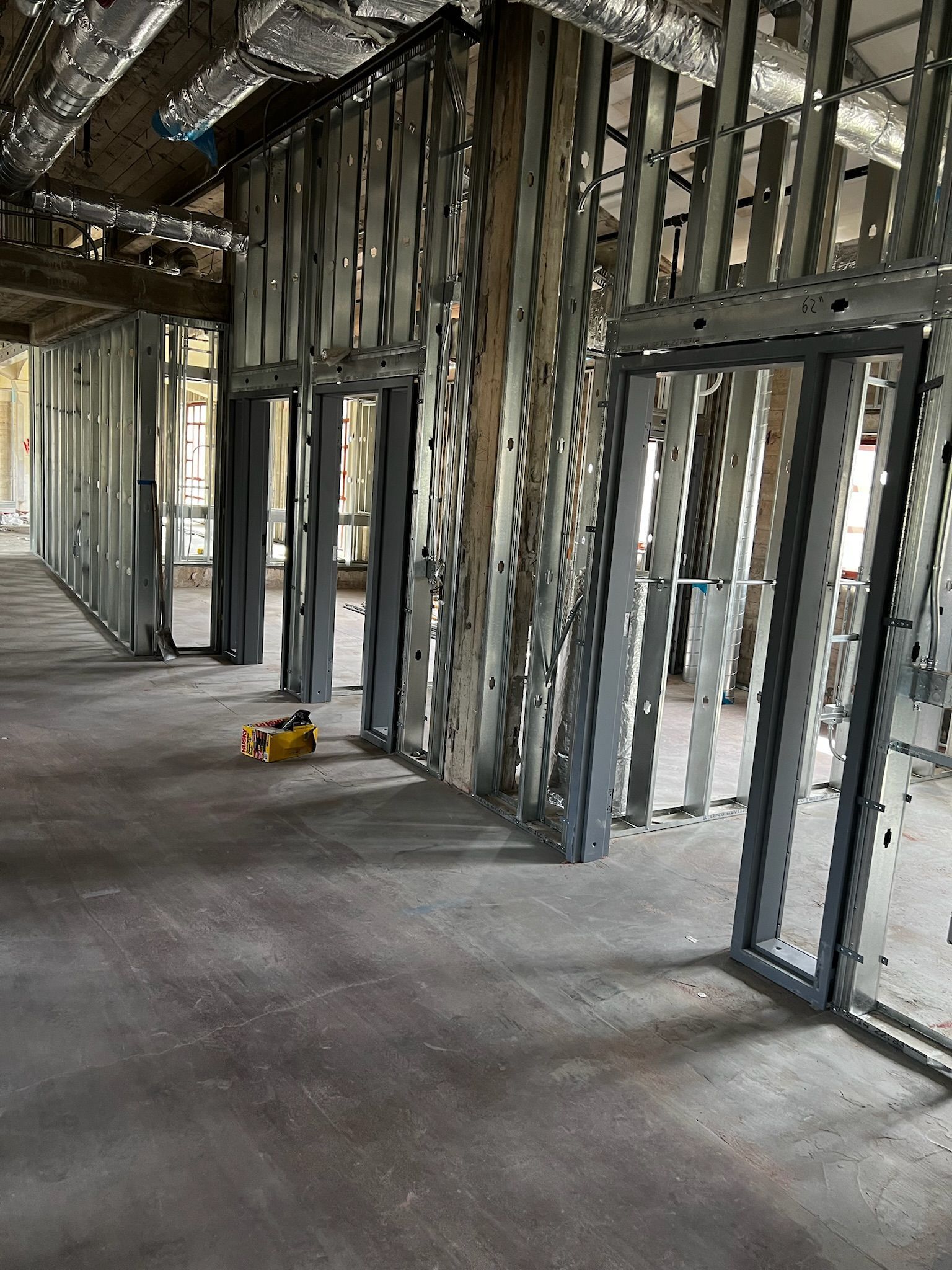 Interior of a building under construction, showing metal framing for walls and doorways, a concrete floor.