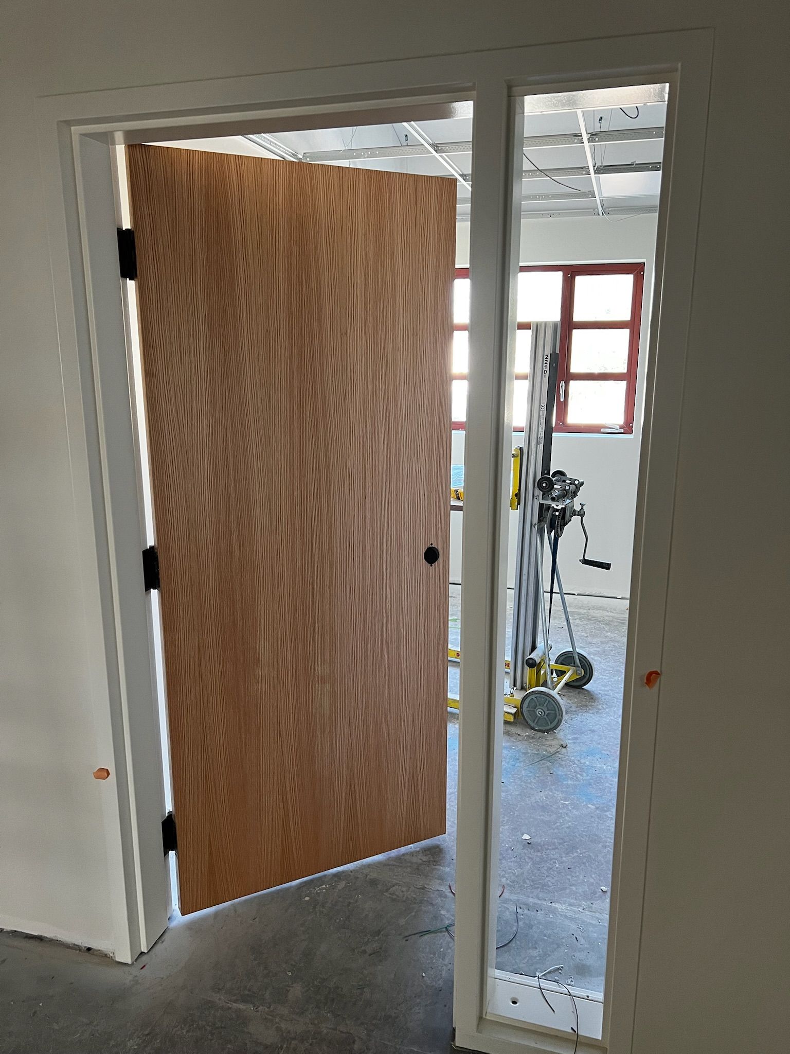 Wooden door, partially open, with black hinges and handle, in a white door frame. Interior view shows unfinished space.