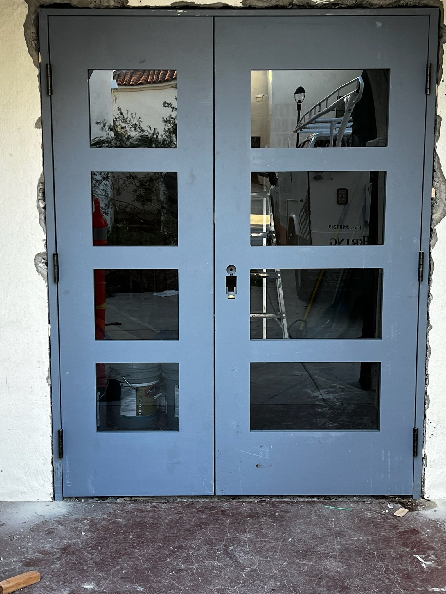 Gray double doors with four rectangular glass panes each, installed in a building entrance.