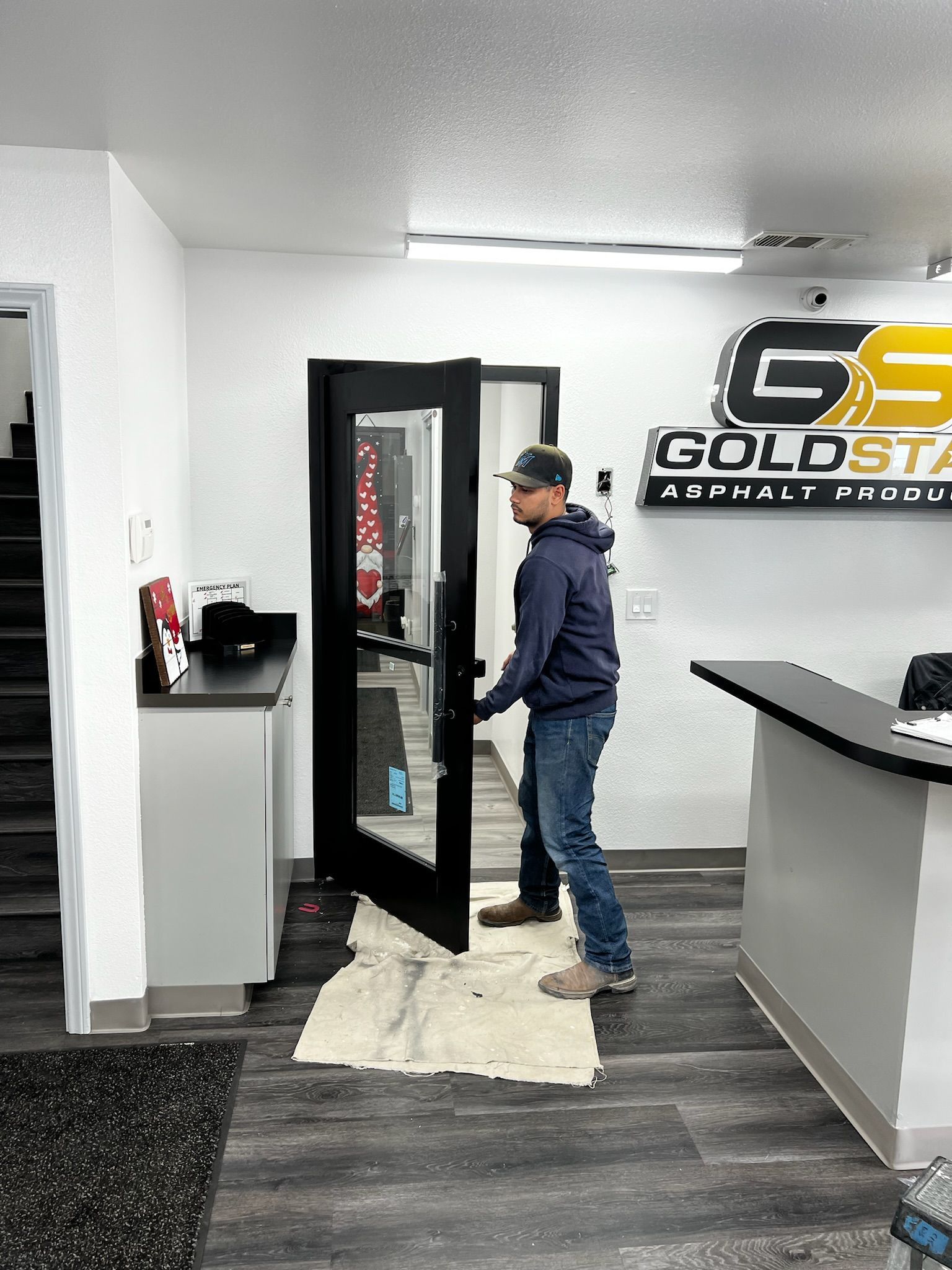 Man opening a black glass door at a Gold Star business. He wears a blue jacket and jeans.