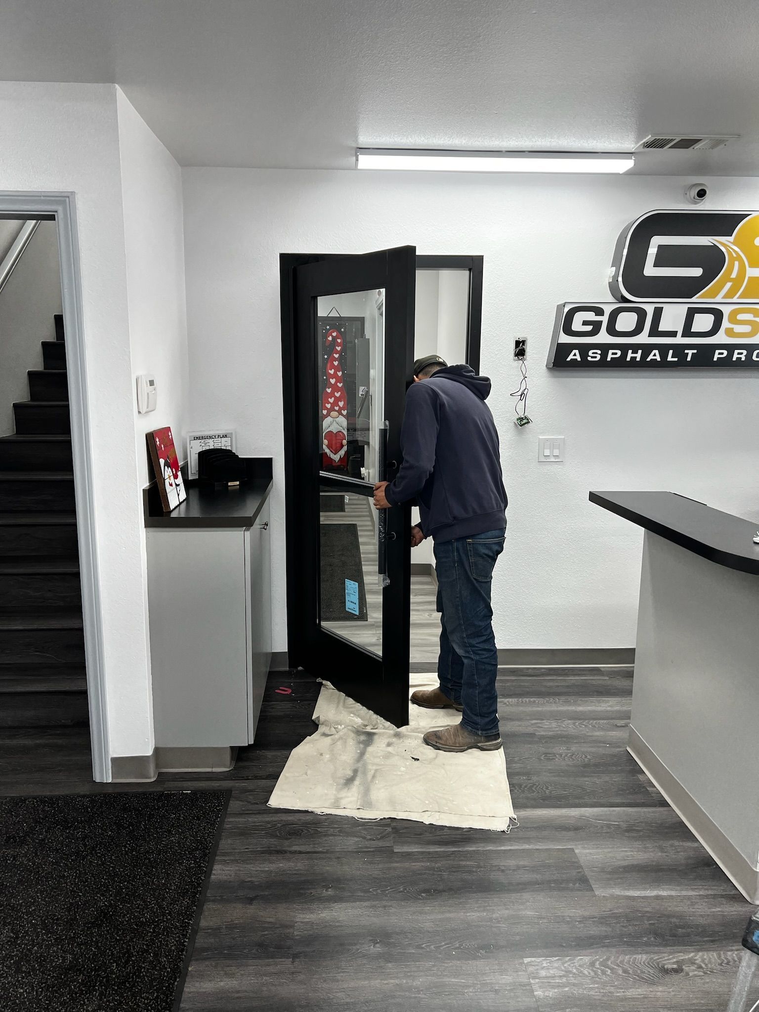 Person installing a black glass door in a commercial space, near a counter and stairs.
