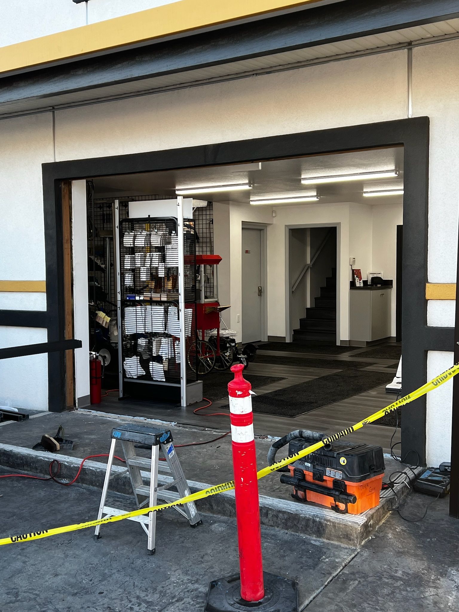 Exterior of a garage with an open door. Safety cones and tools are present. Yellow caution tape.