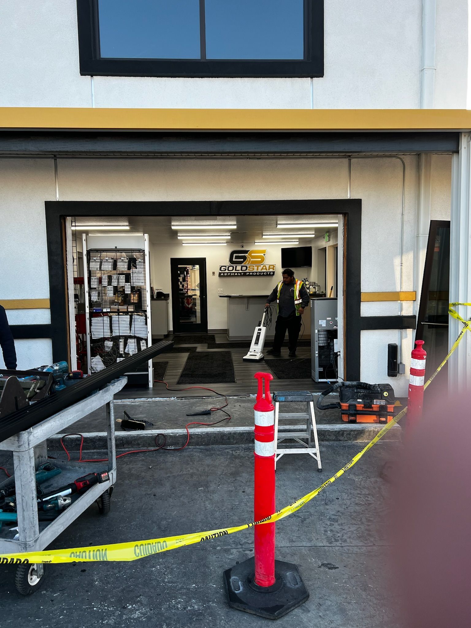 Open garage with work area; caution tape, red/white post.