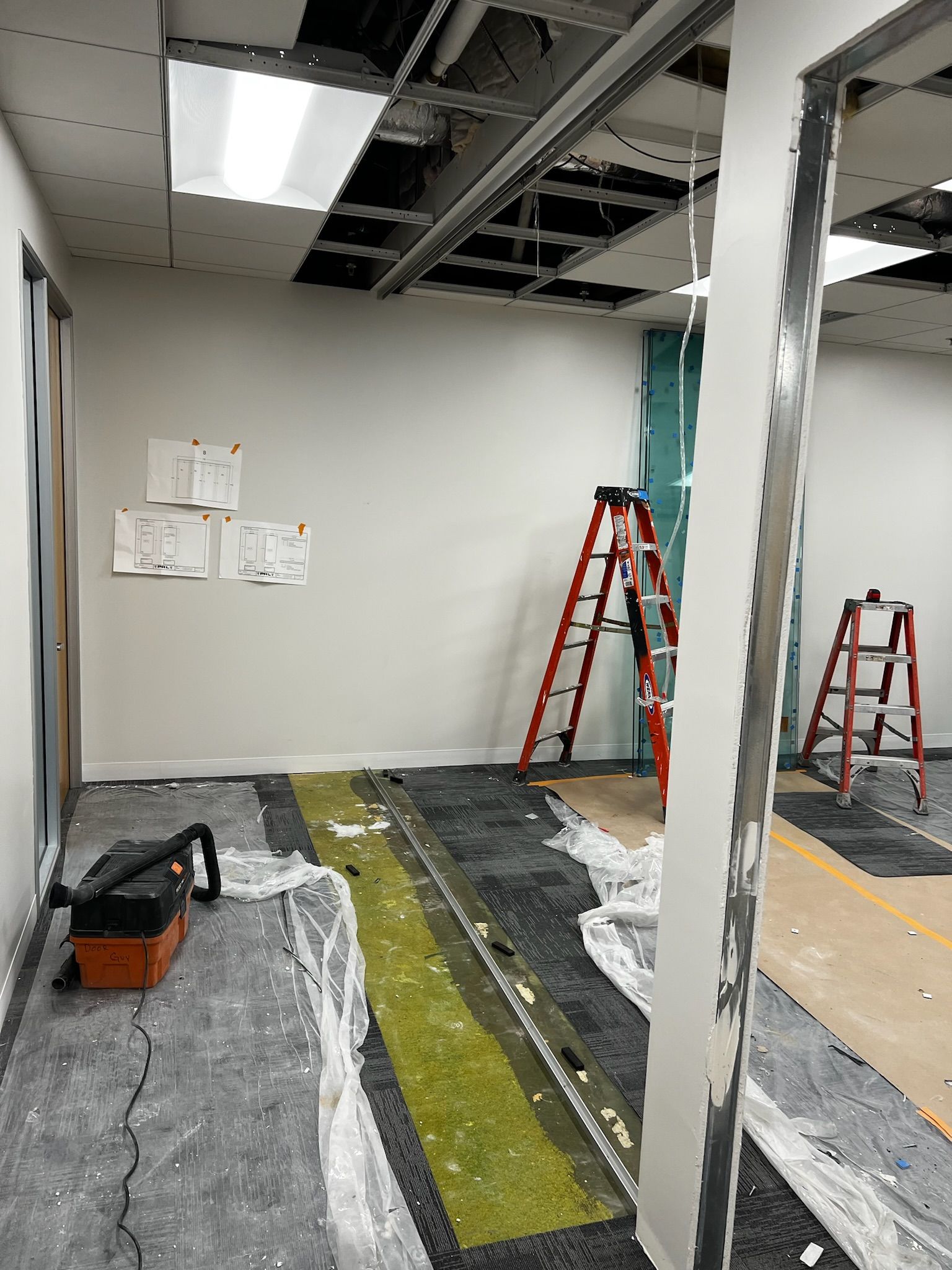 Office under construction; exposed ceiling, tools, two ladders, unfinished walls and flooring.