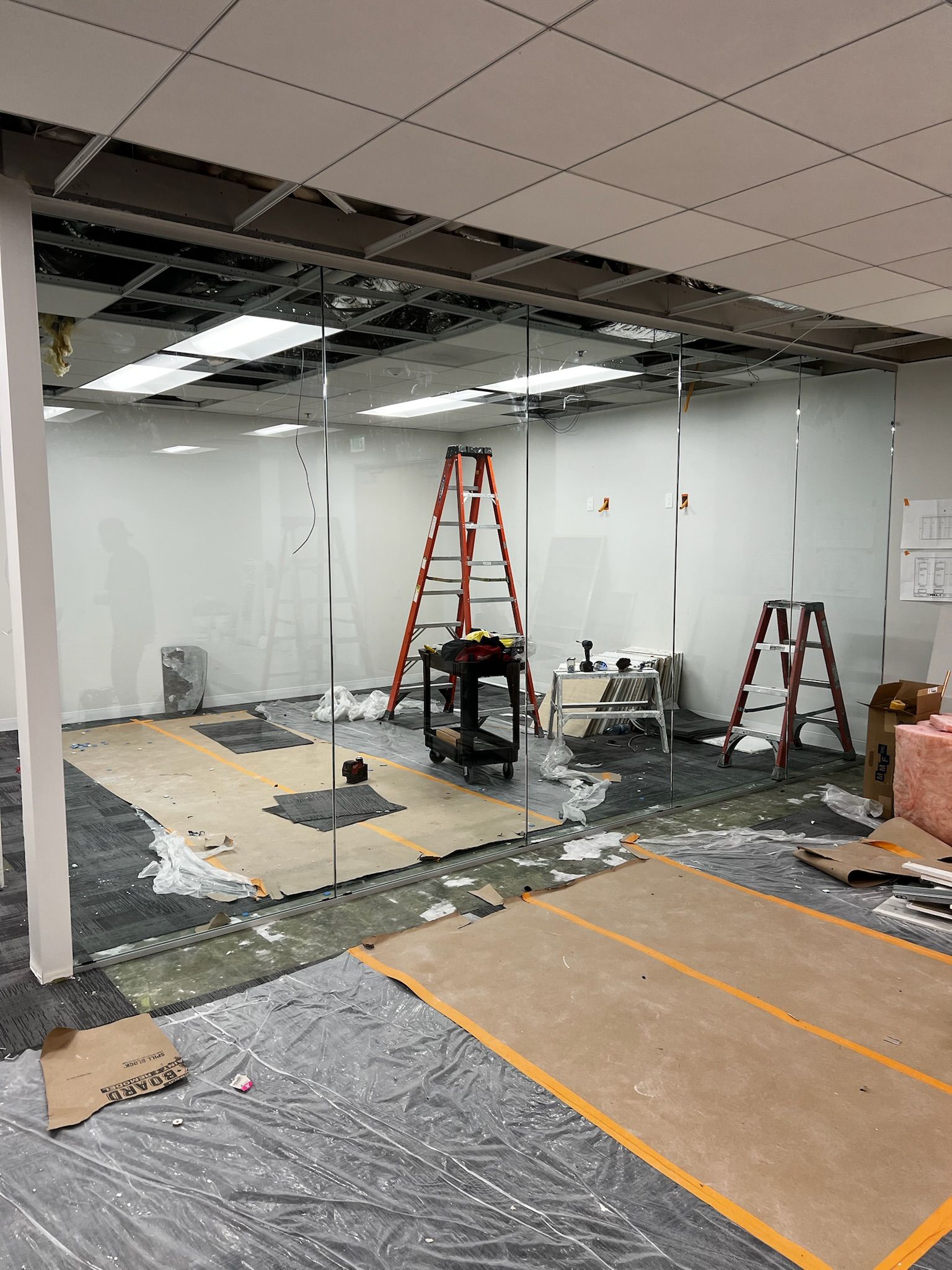 Office interior during renovation. Damaged ceiling, ladders, glass walls, covered floor.