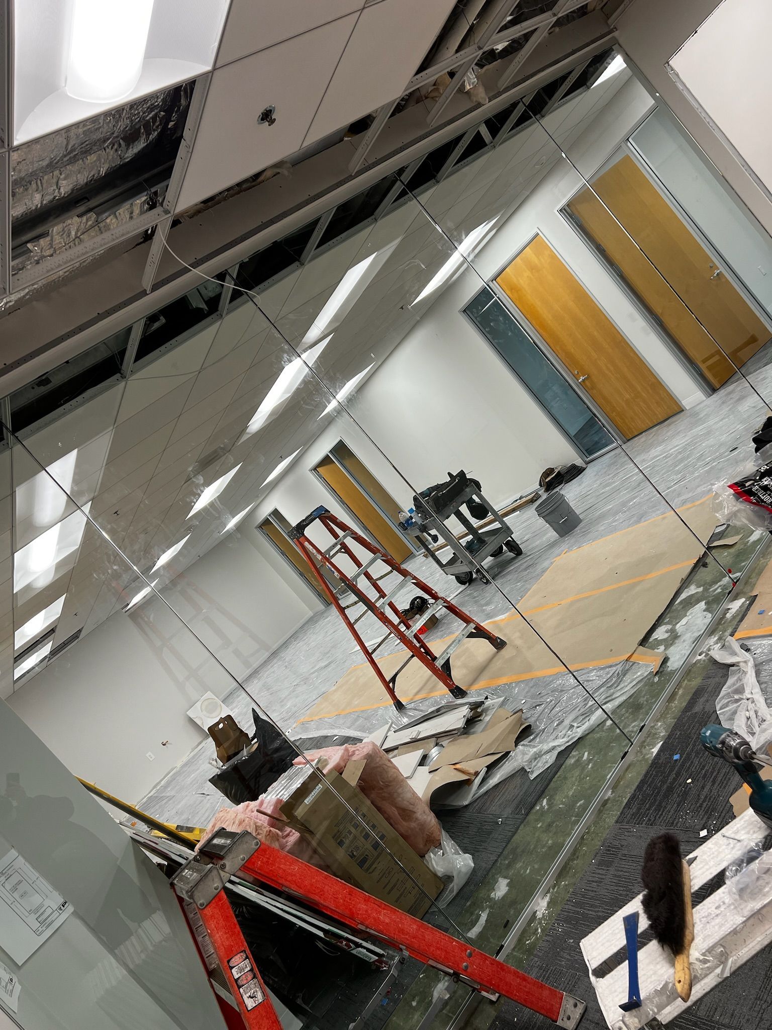 Interior view of a room under renovation. Ceiling tiles and debris scattered; a ladder and tools are present.