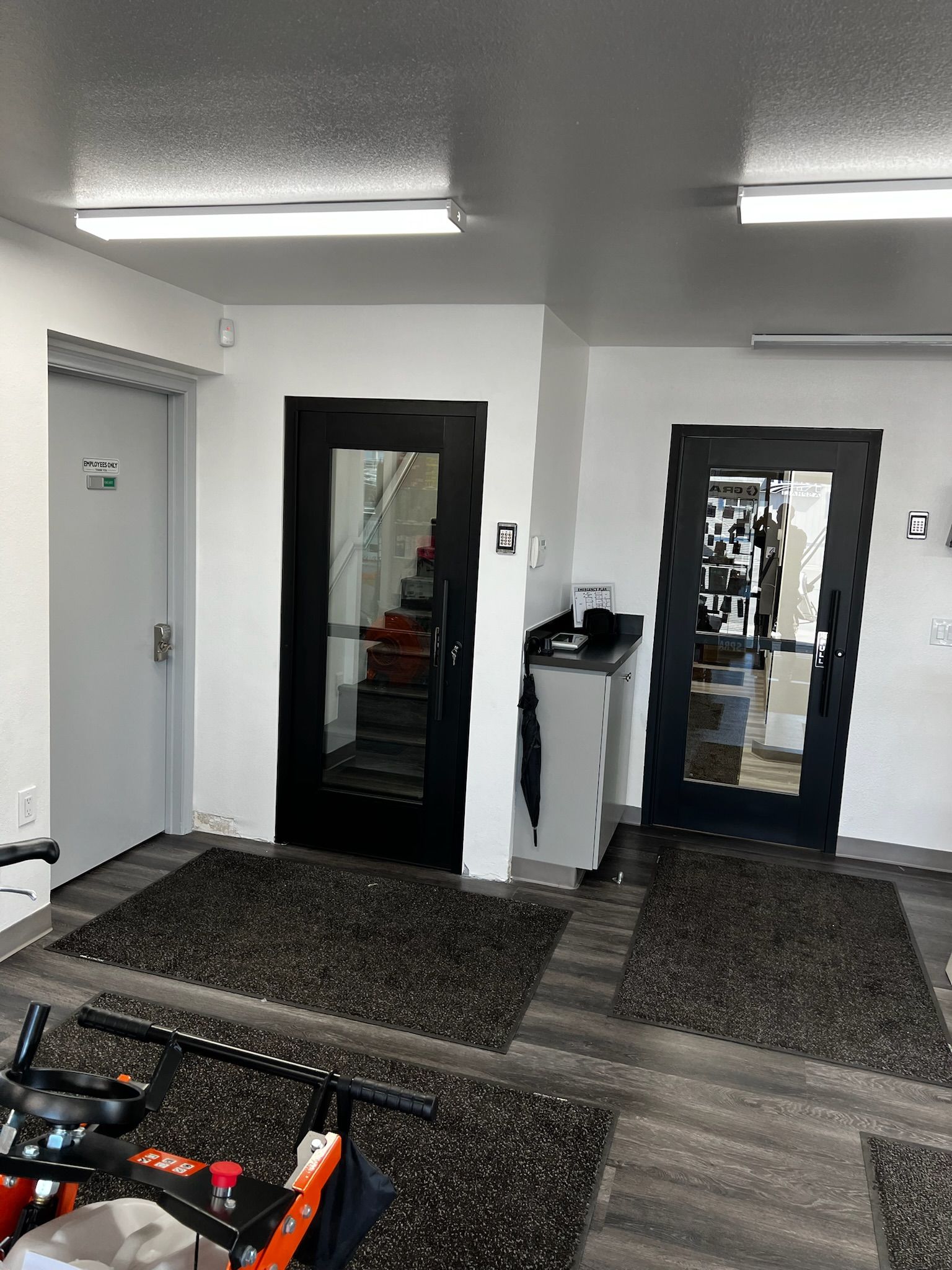 An interior view of a commercial space. Features three doors, dark floor mats, and overhead lighting.