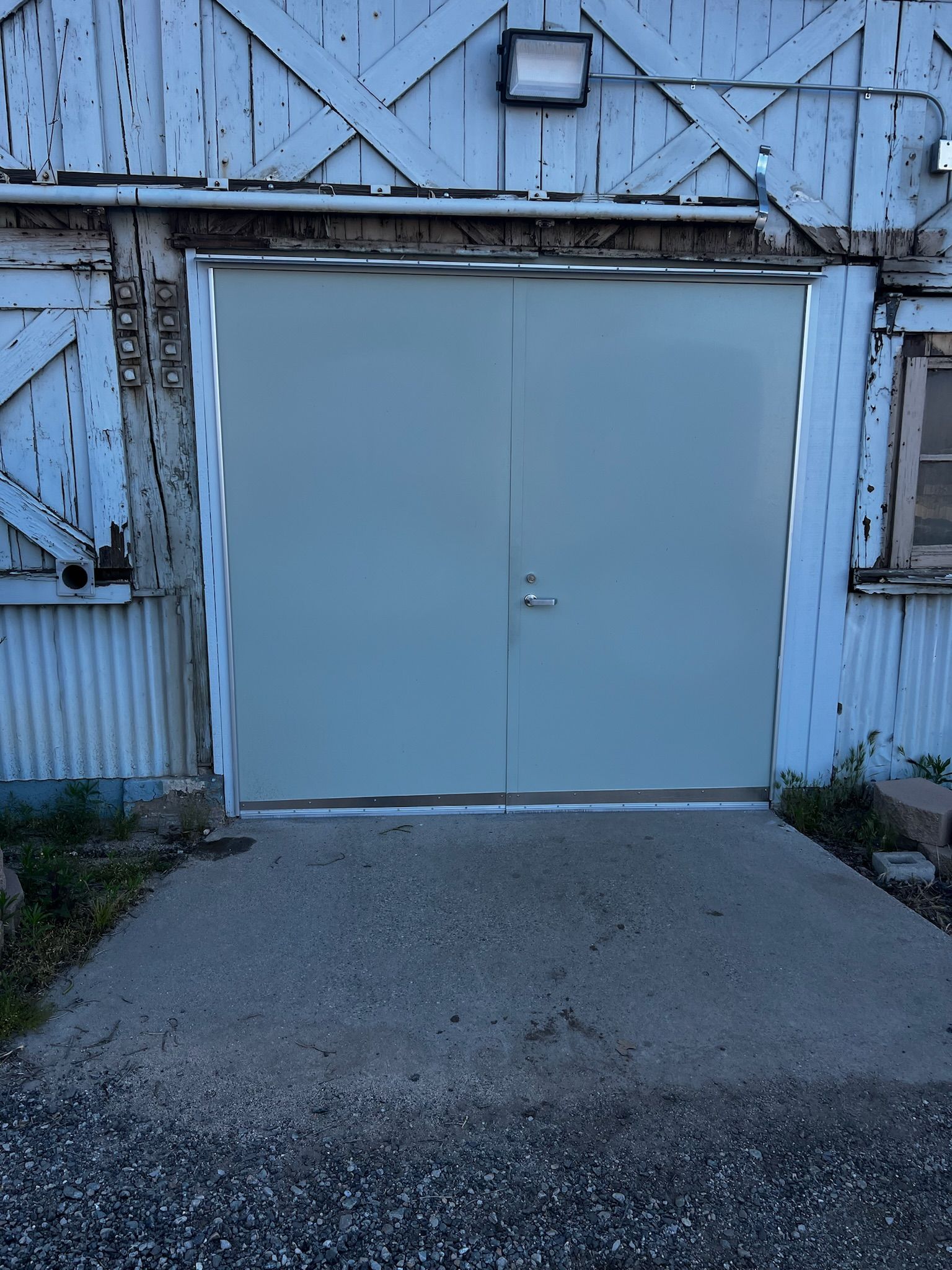 Gray double doors in a weathered, white building with a concrete ramp leading up to the entrance.