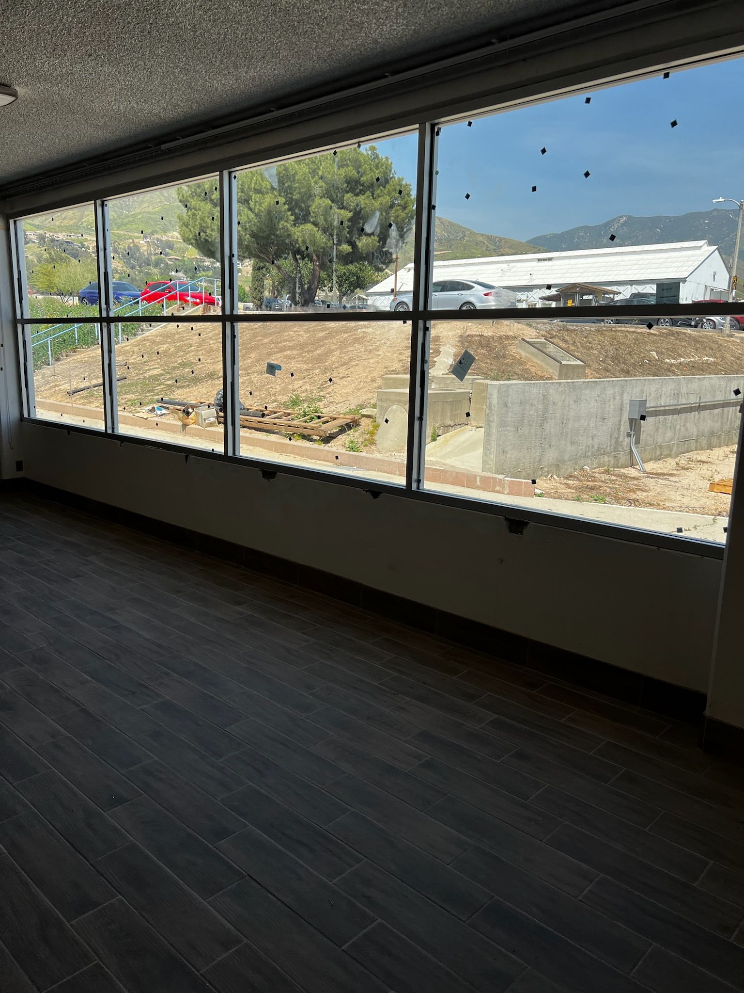 Interior view through a large window. Shows dark floor, bright outdoor scene with trees and buildings.