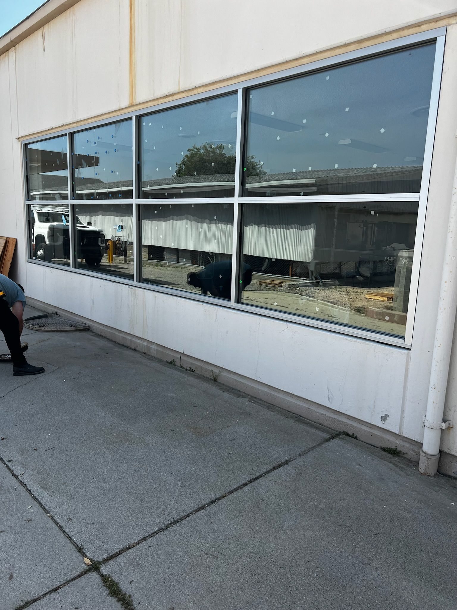 Exterior of a building with a long window reflecting a yard and sky; a person stands nearby.