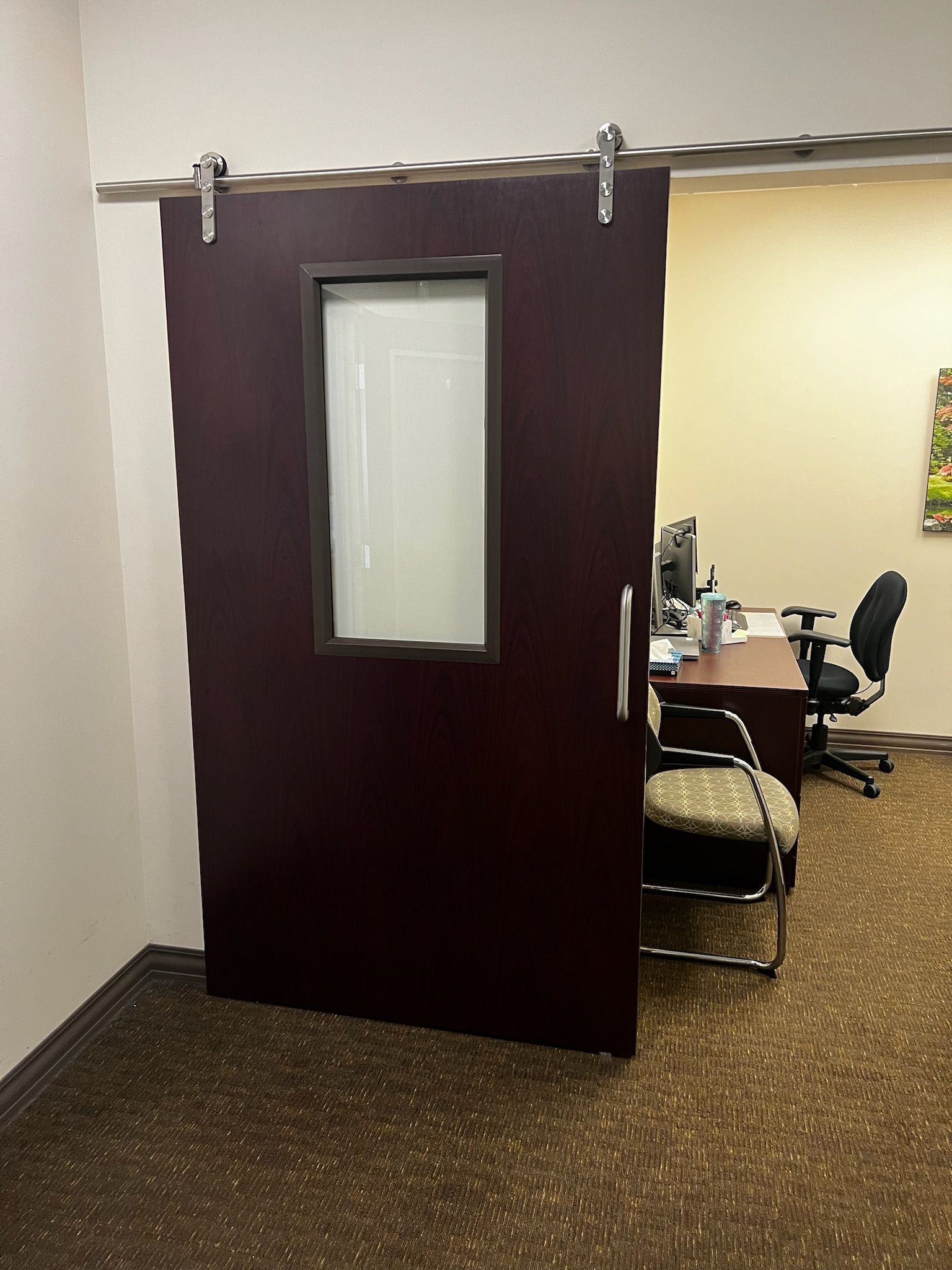Dark sliding door with window, leading to office with desk and chair.