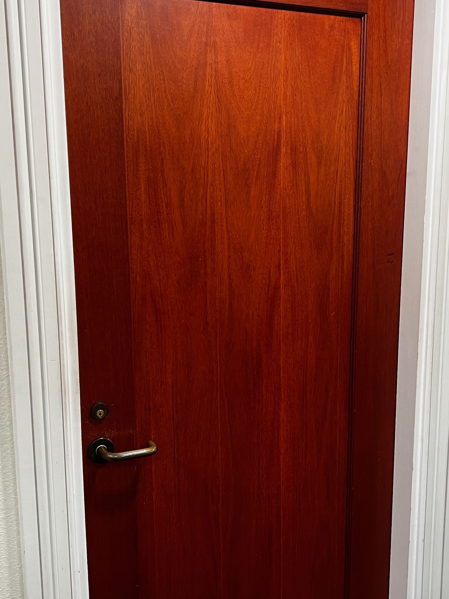Wooden door with dark red finish and silver handle, set within a white doorway.