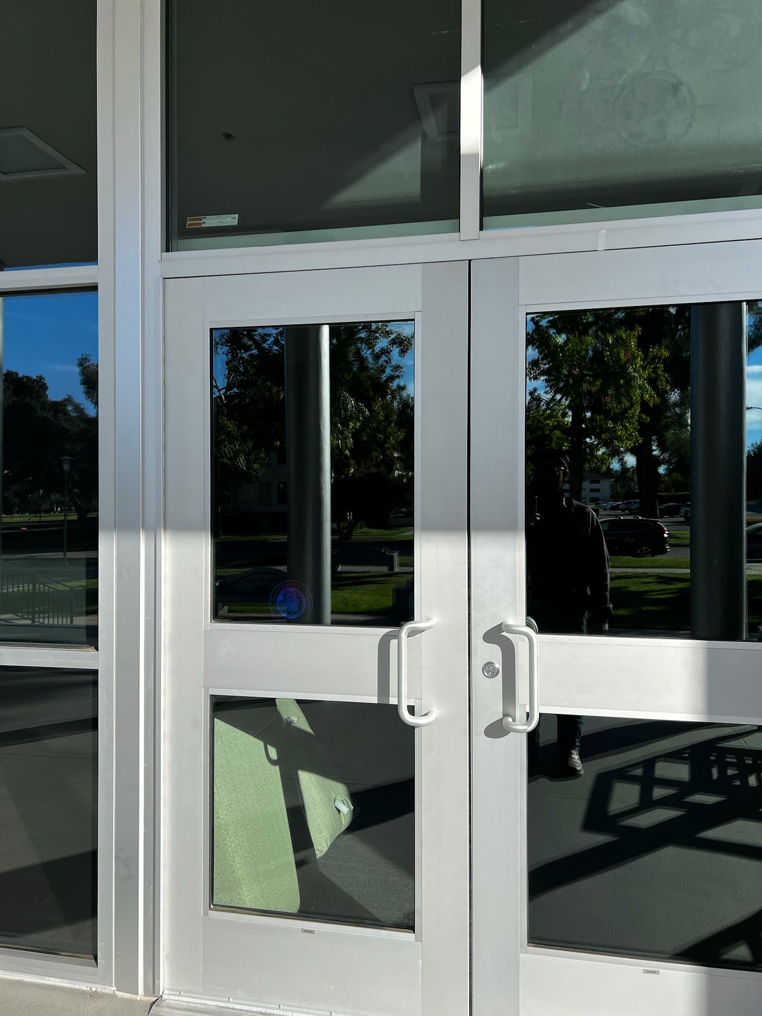 Silver double doors with glass panels reflecting a green yard and trees.