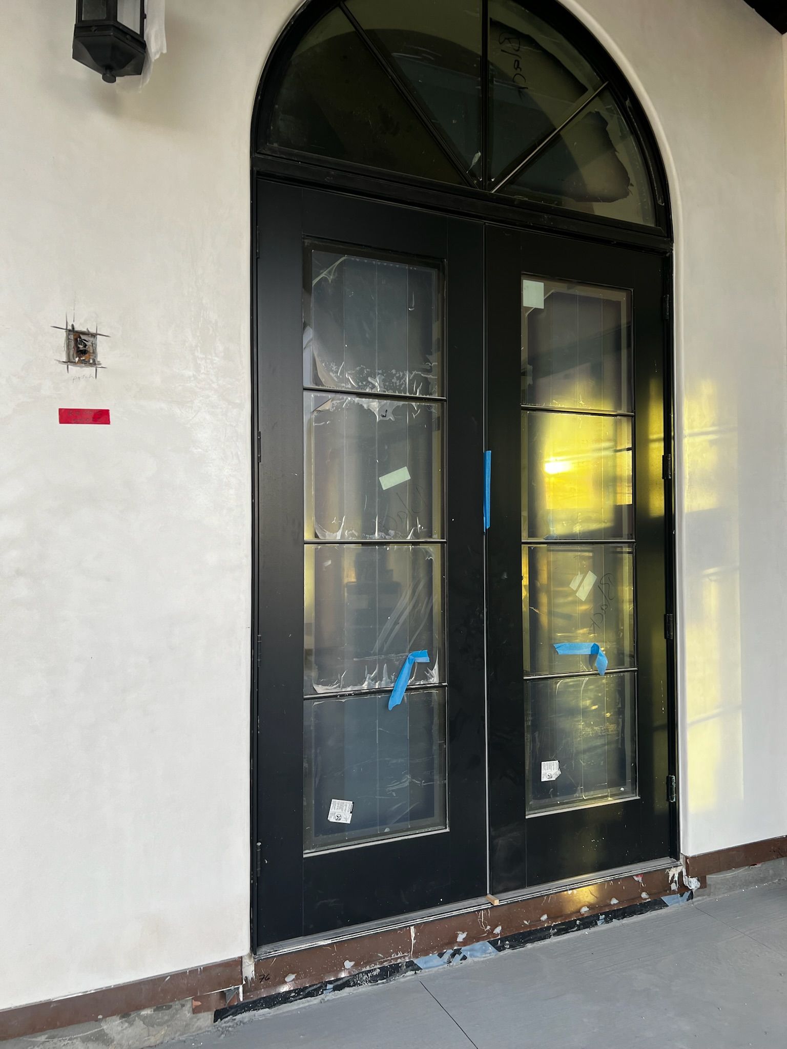 Black arched double doors with glass panels on a white building, under construction.