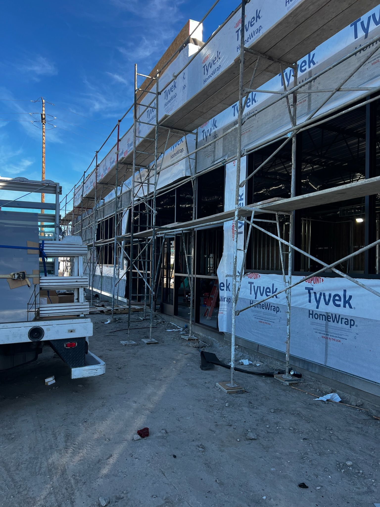 Building under construction with scaffolding and a truck in the foreground, under a blue sky.