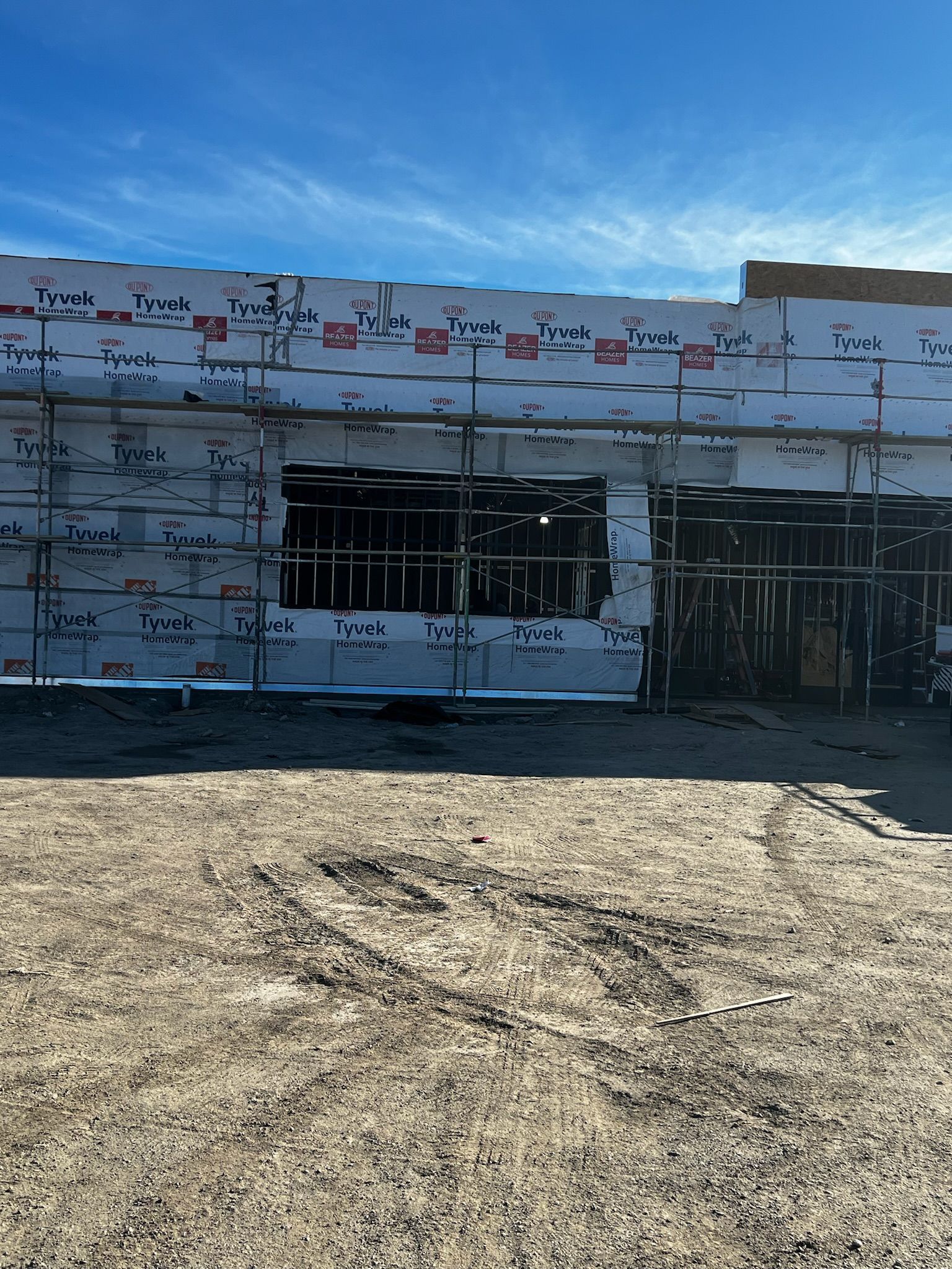 Building exterior under construction with exposed framing and sheathing, set against a clear blue sky.