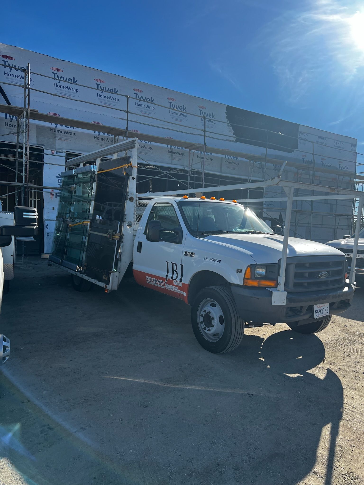 White work truck parked outdoors under a blue sky, with metal framework and cargo.