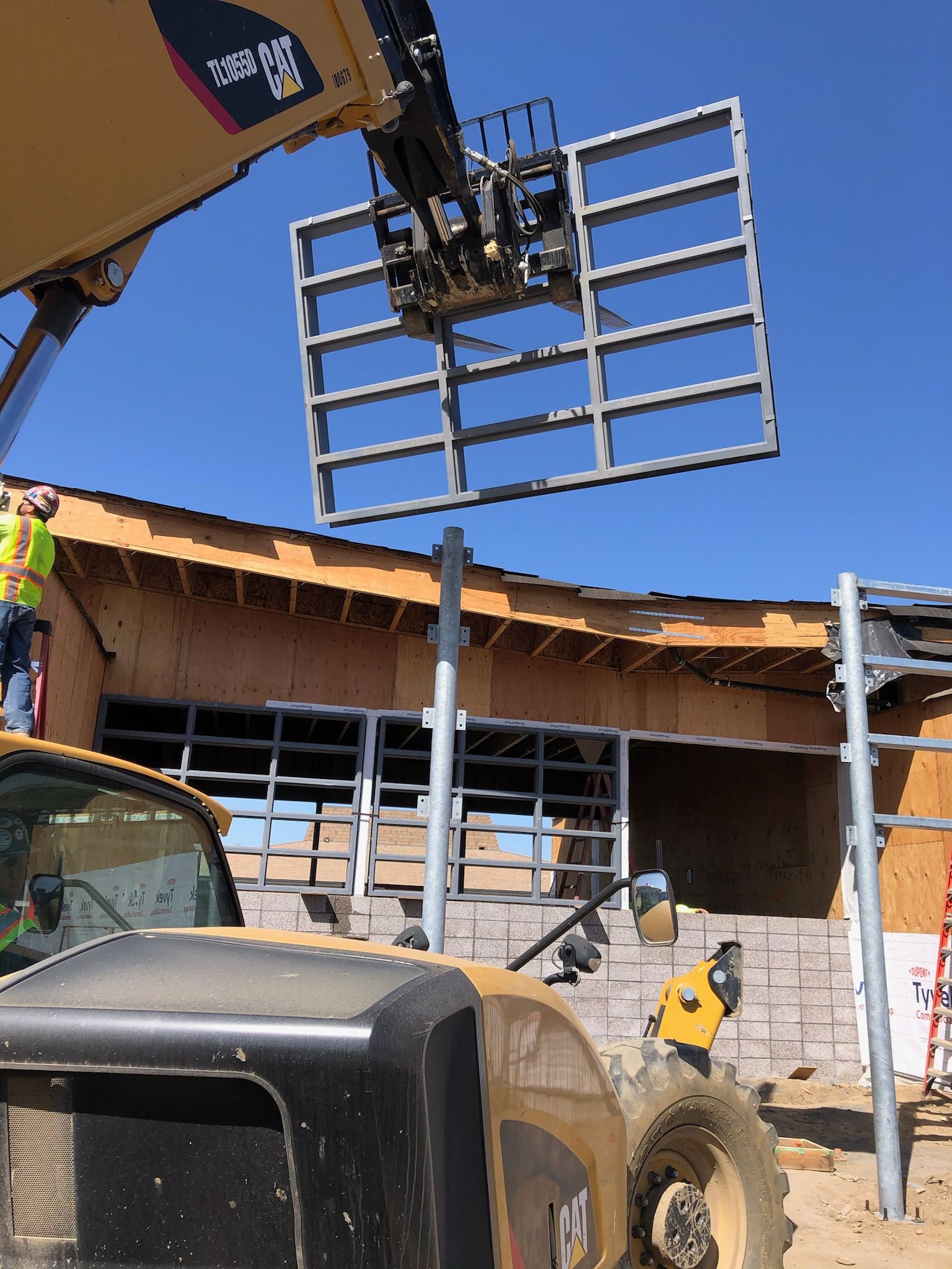 A construction worker uses a forklift to lift a metal frame, possibly a window. Sunny day.