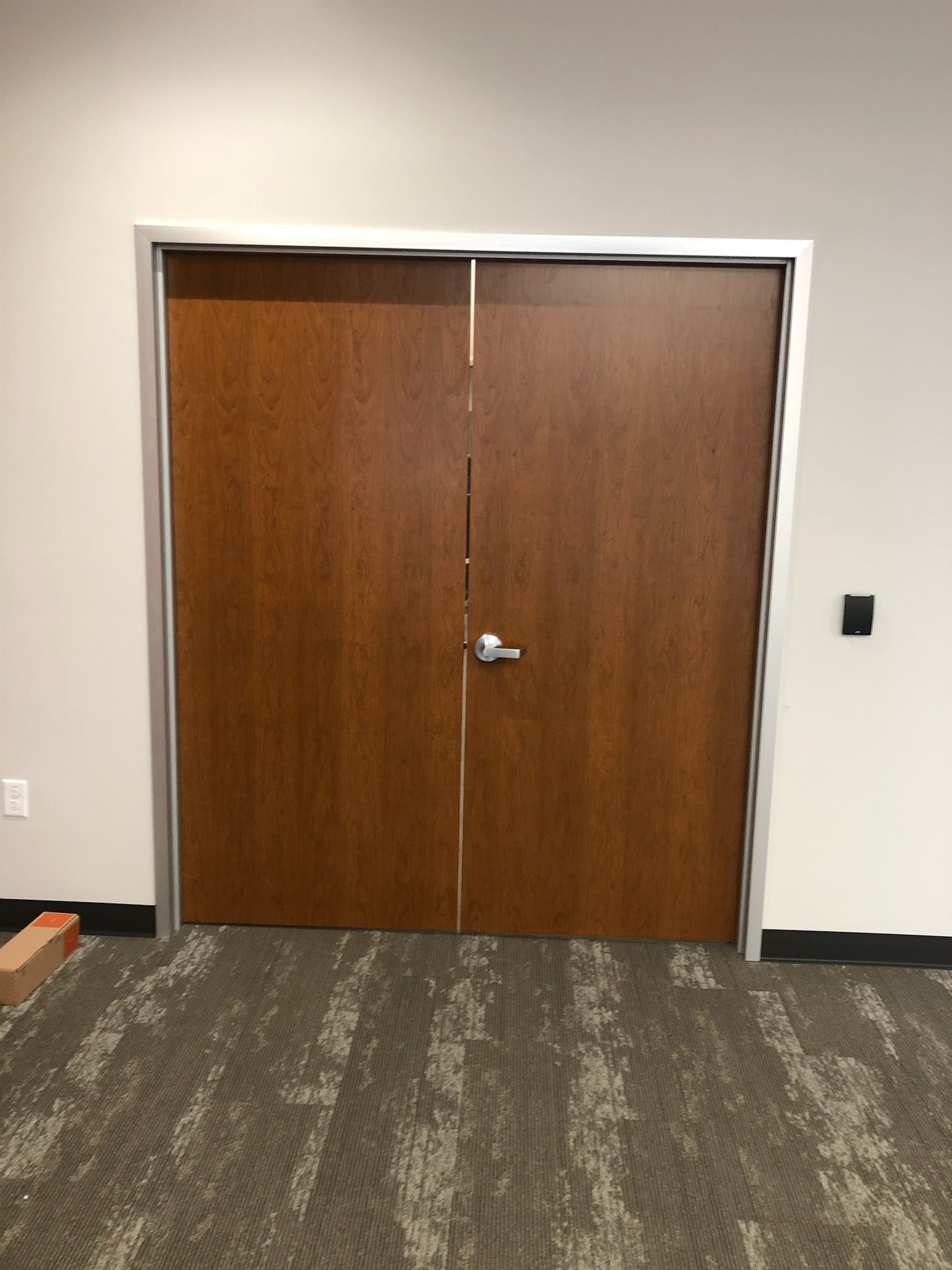Brown double doors with silver frame in a room with carpet flooring and light gray walls.