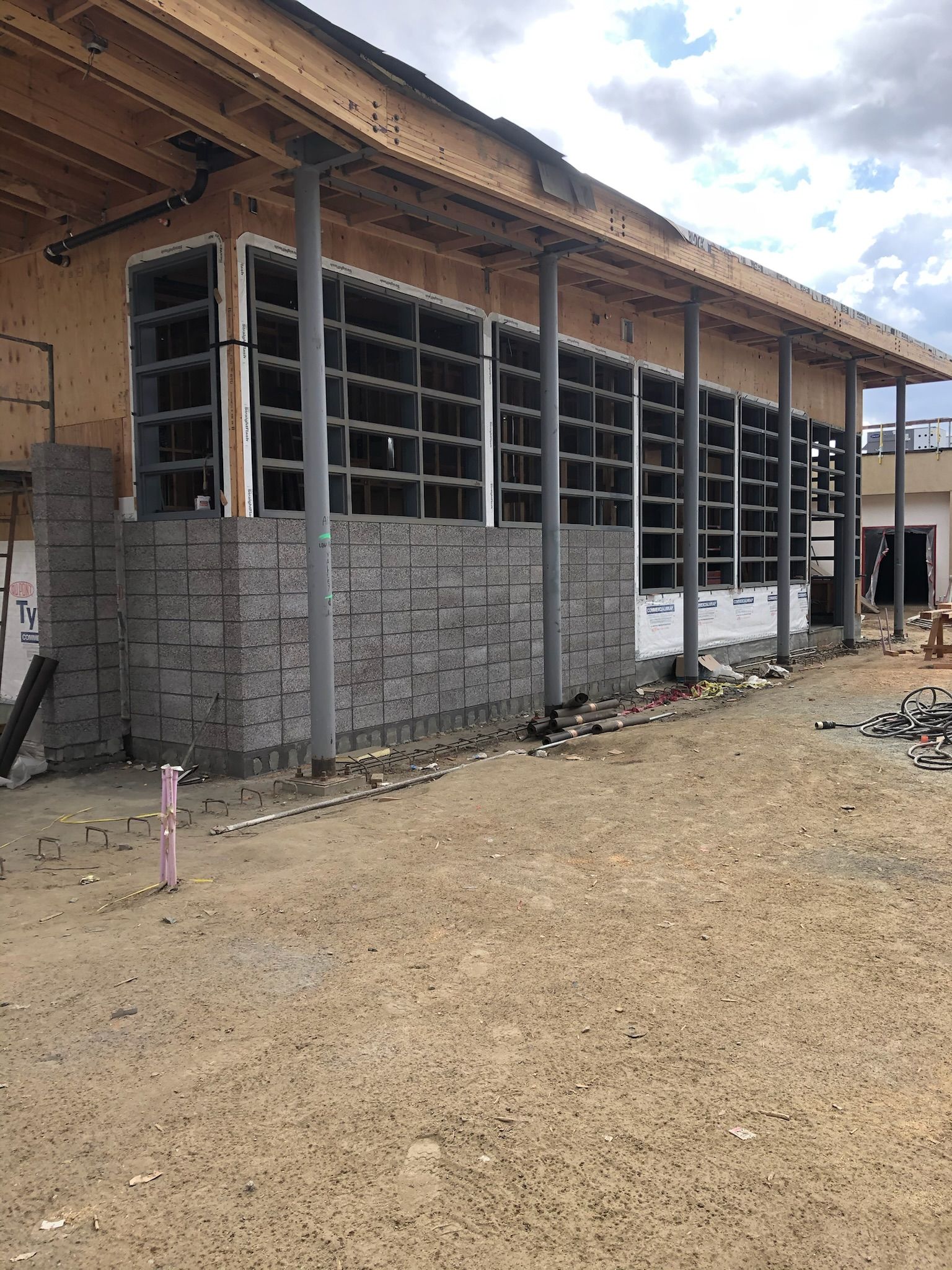 Building exterior under construction with exposed wood, gray stone facade, and large window openings.