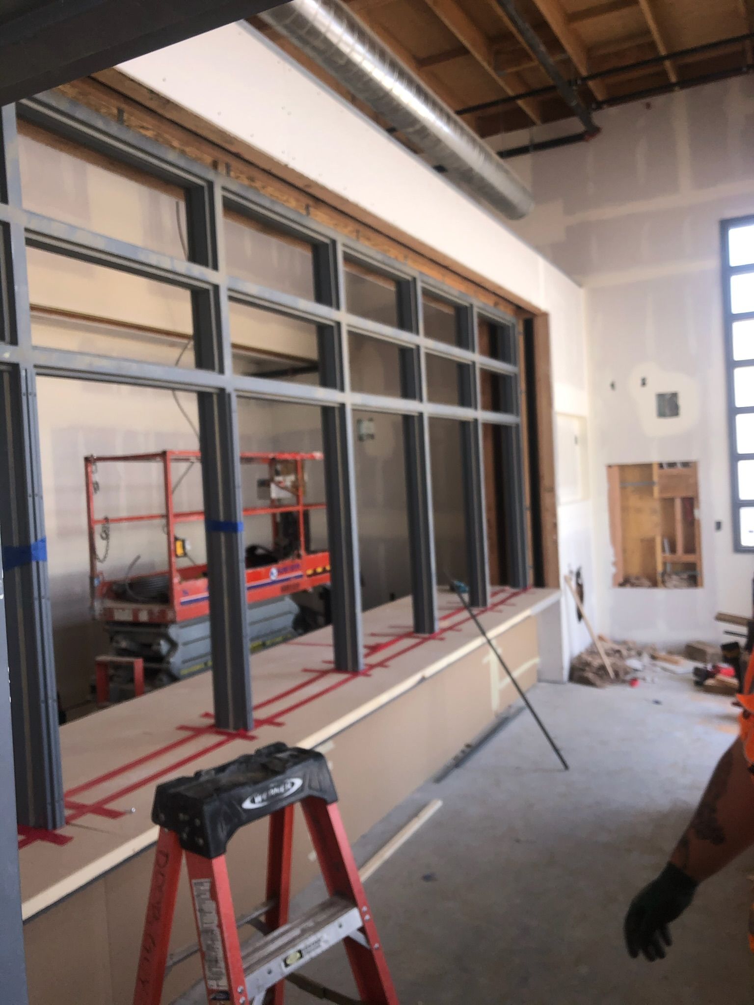Interior construction site with metal-framed windows, red ladder, and drywall.