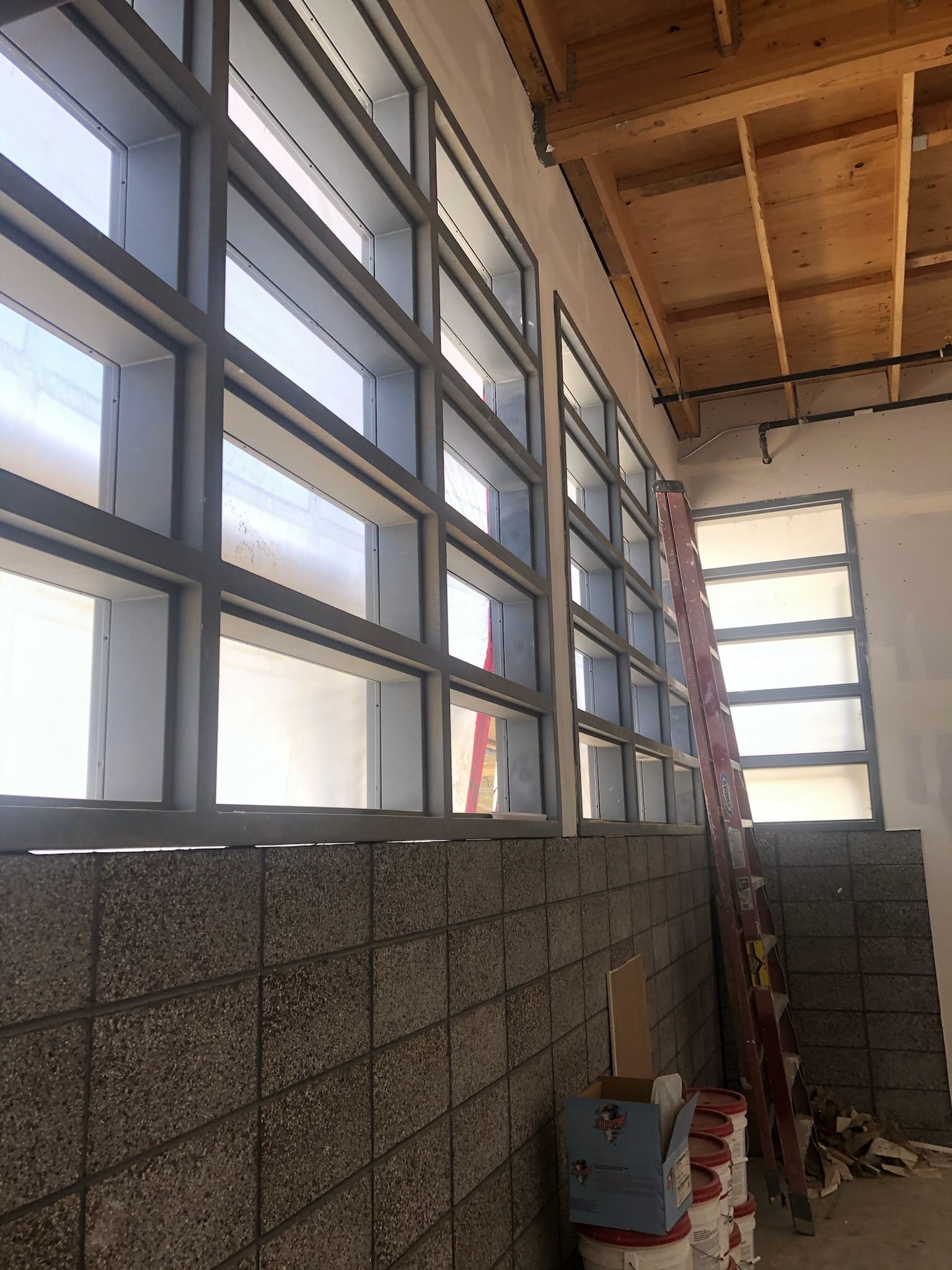 Interior view of a building under construction. Concrete block wall, large windows, wood ceiling.