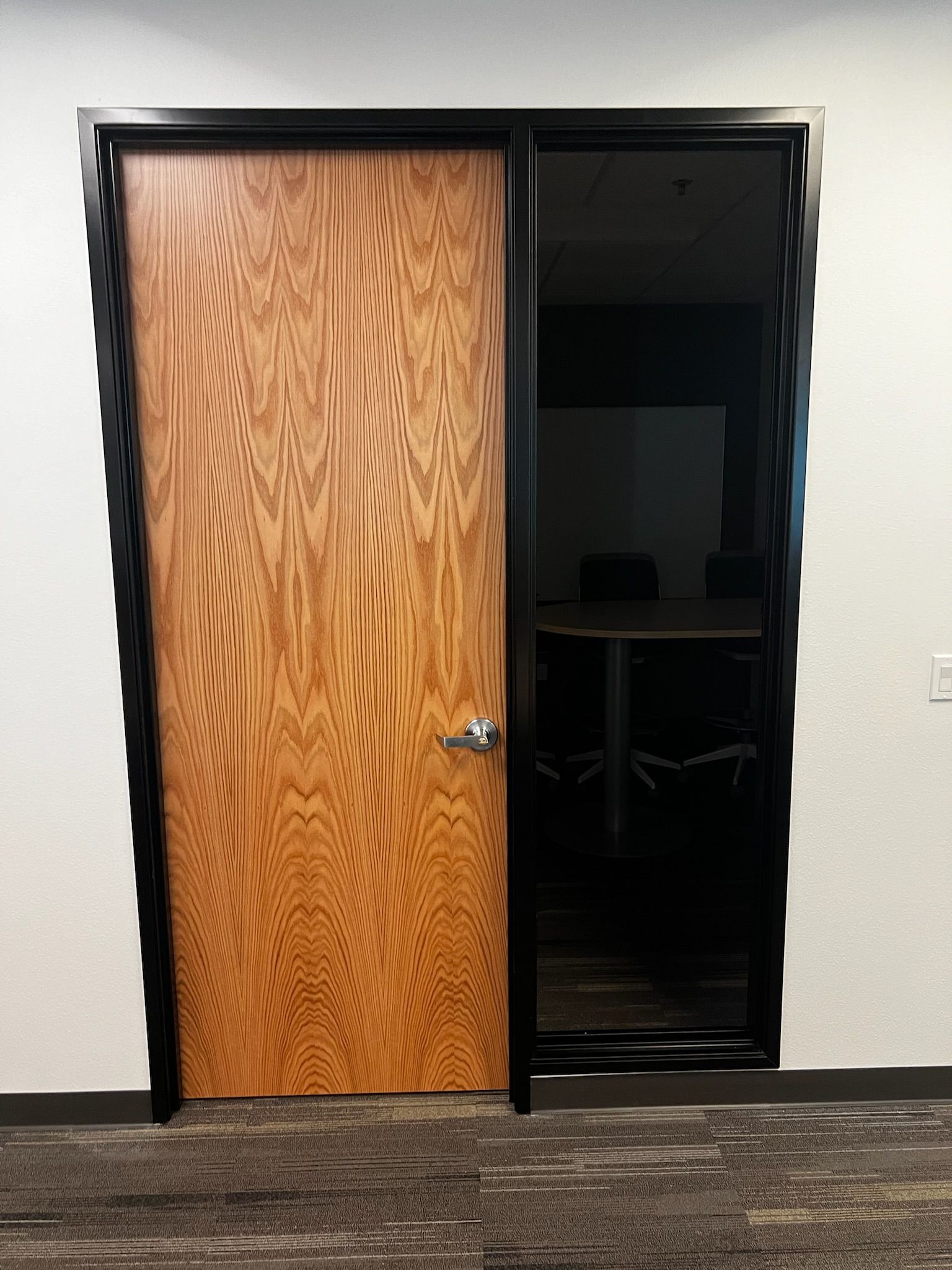 Wooden door and dark glass panel in black frame, set in white wall with carpet floor.
