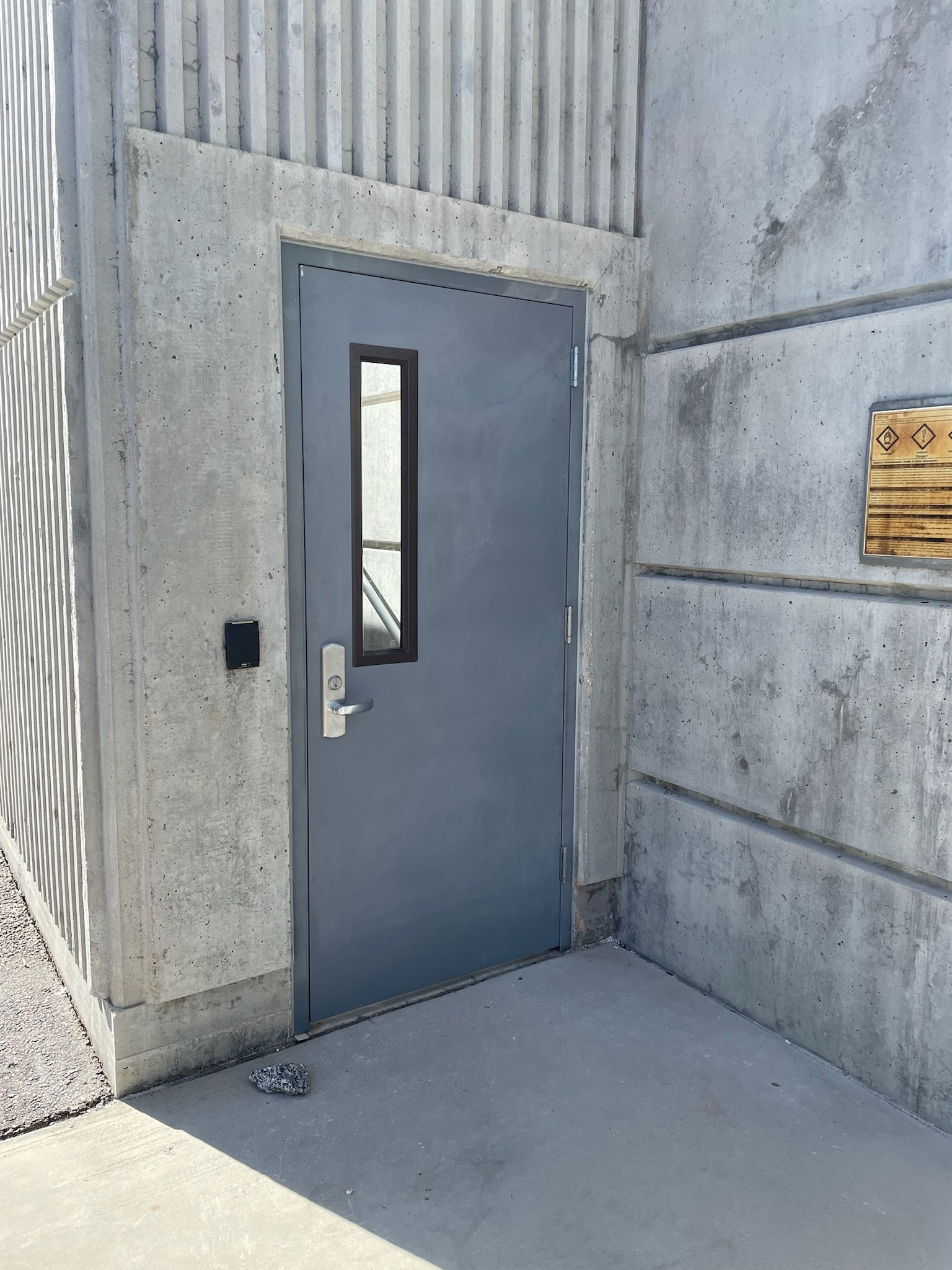 Gray door with window, set in concrete wall with a sign.