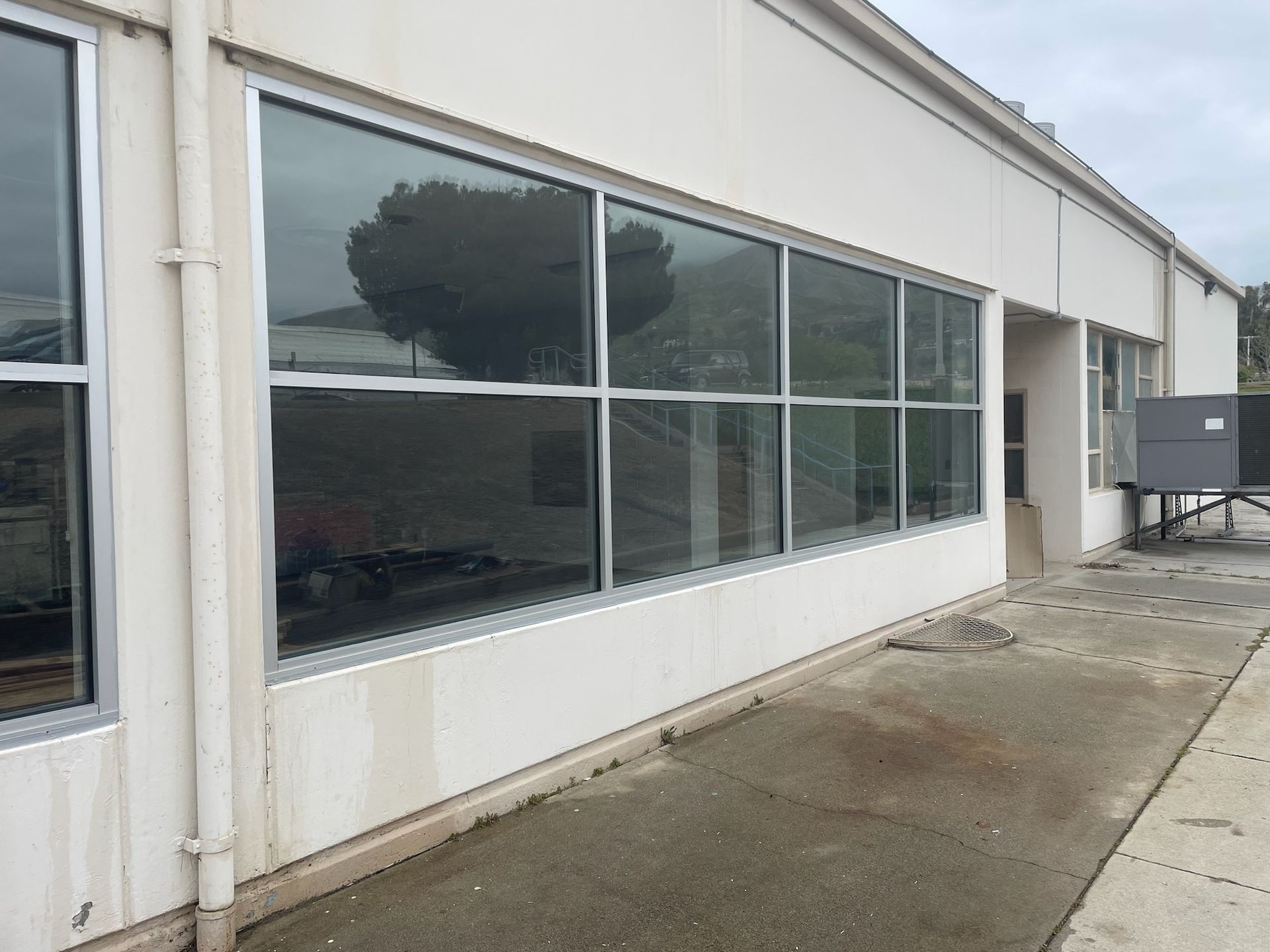 Exterior view of a building with large rectangular windows reflecting the sky and trees, on a gray day.