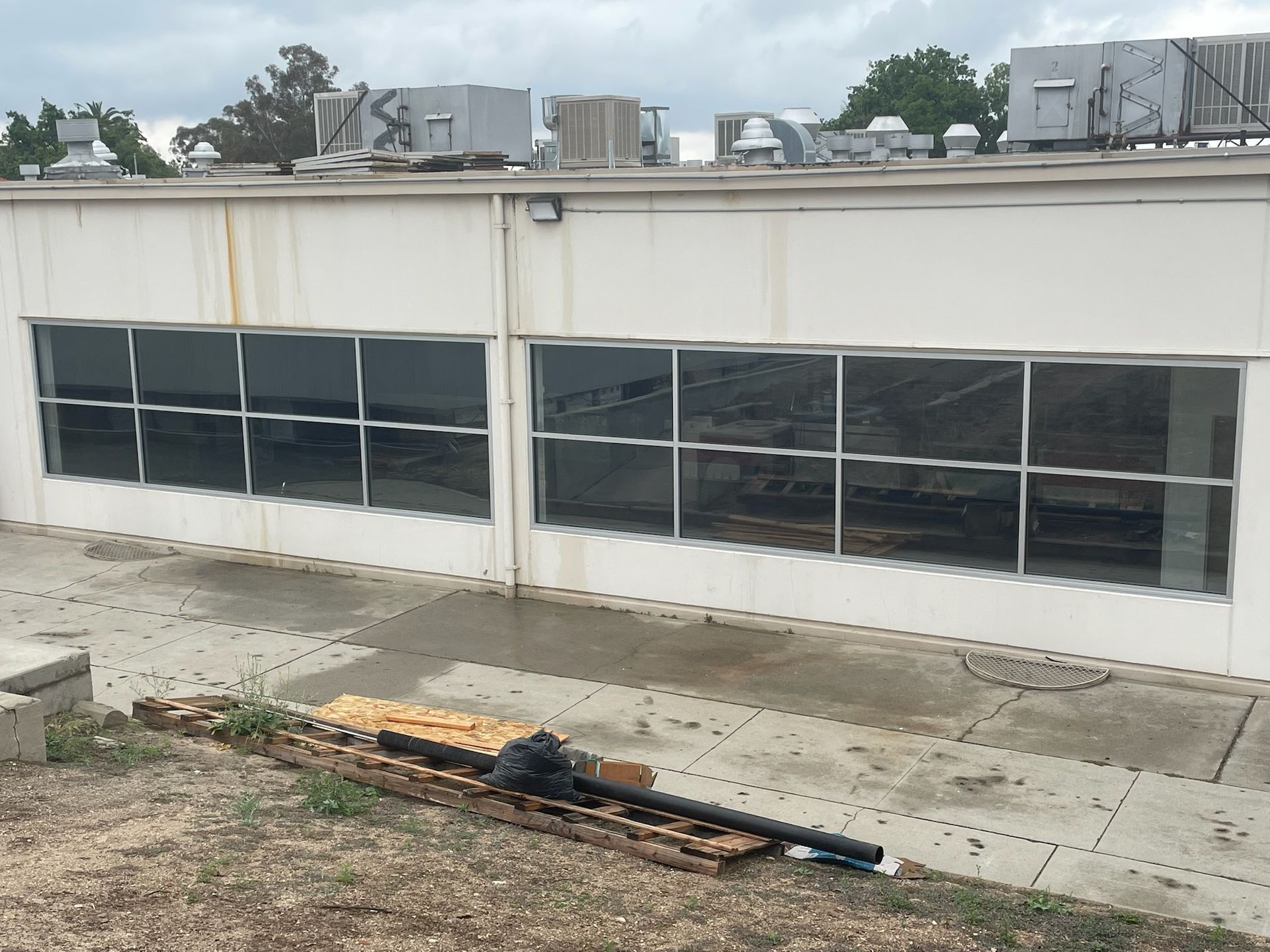 A white building with large windows and rooftop equipment; construction materials lie in front.
