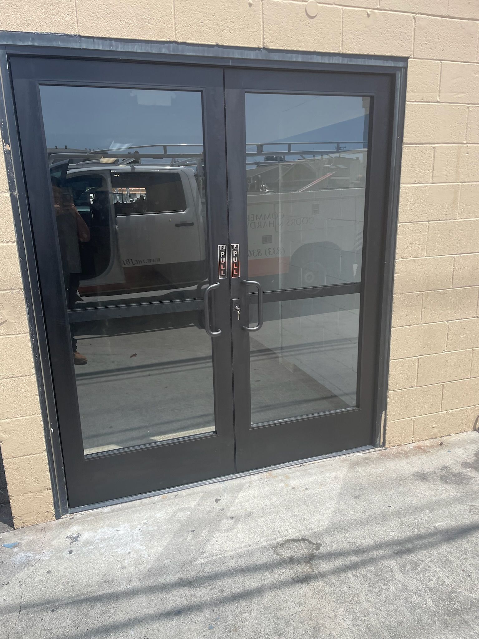Double glass doors with dark frames, reflecting vehicles in parking lot.