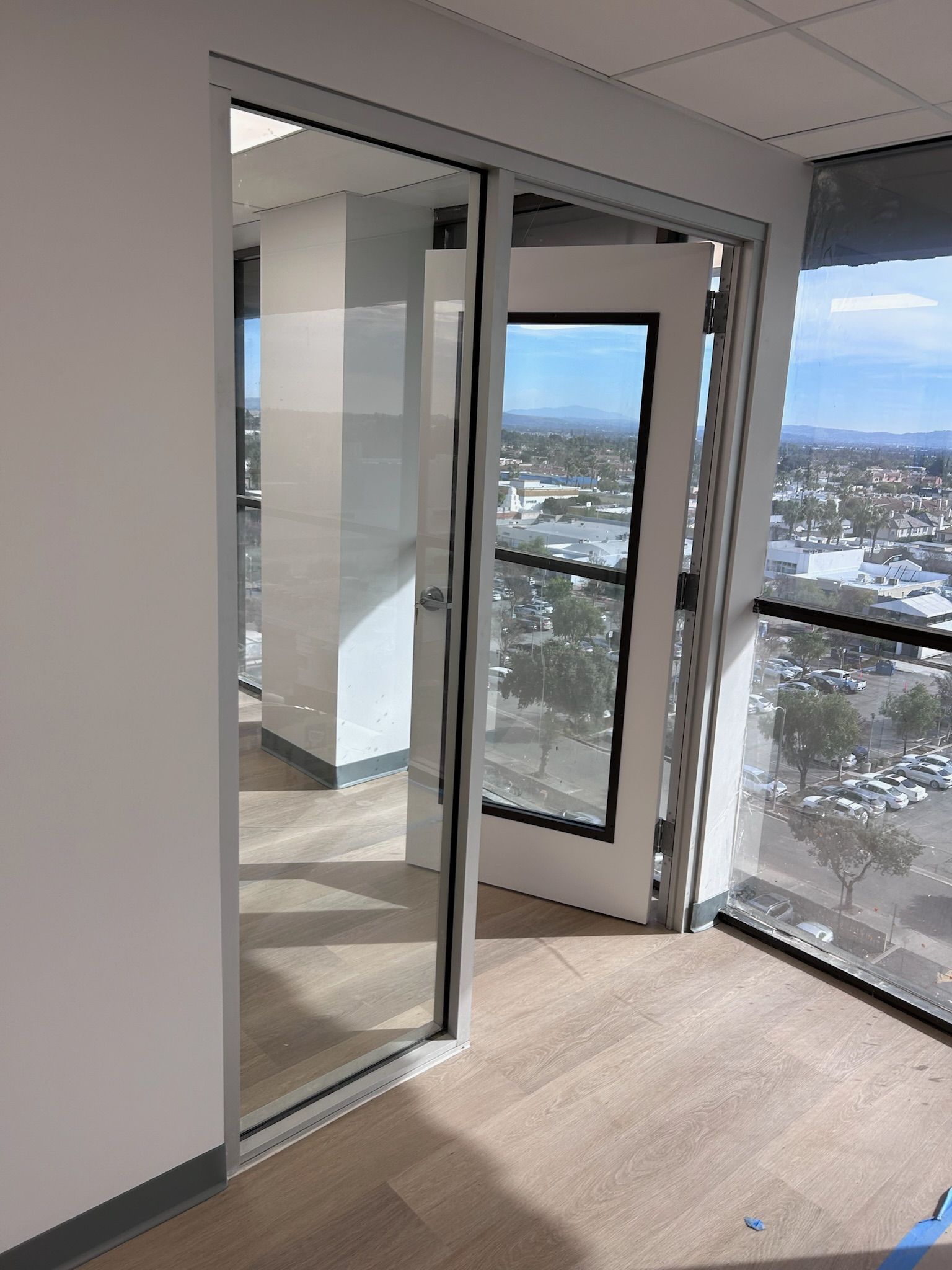 Open glass doors leading to a balcony with city views. Light wood floor, white walls and trim.
