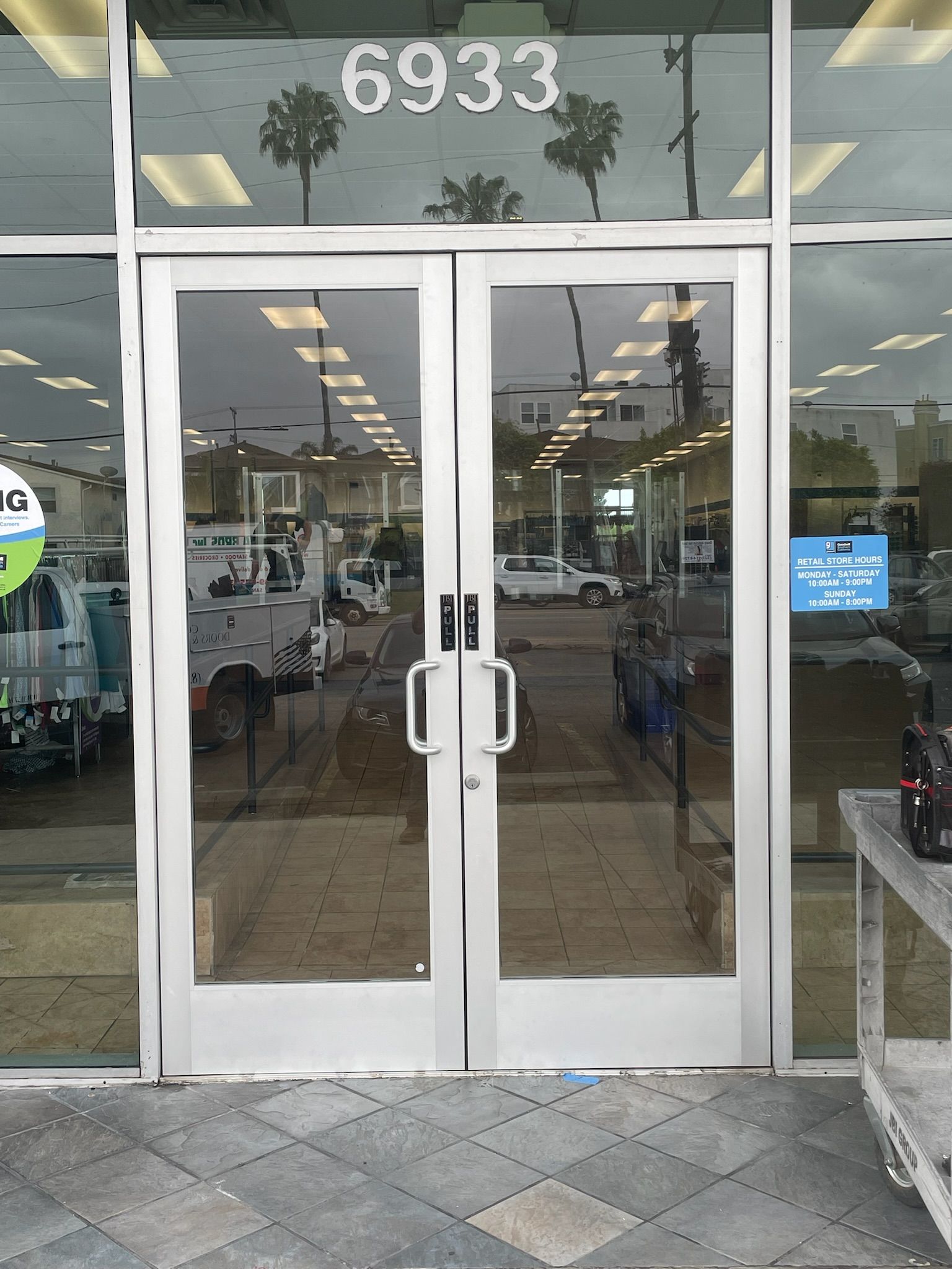 Double doors with handles, building number 6933 above, reflecting exterior, white trim.