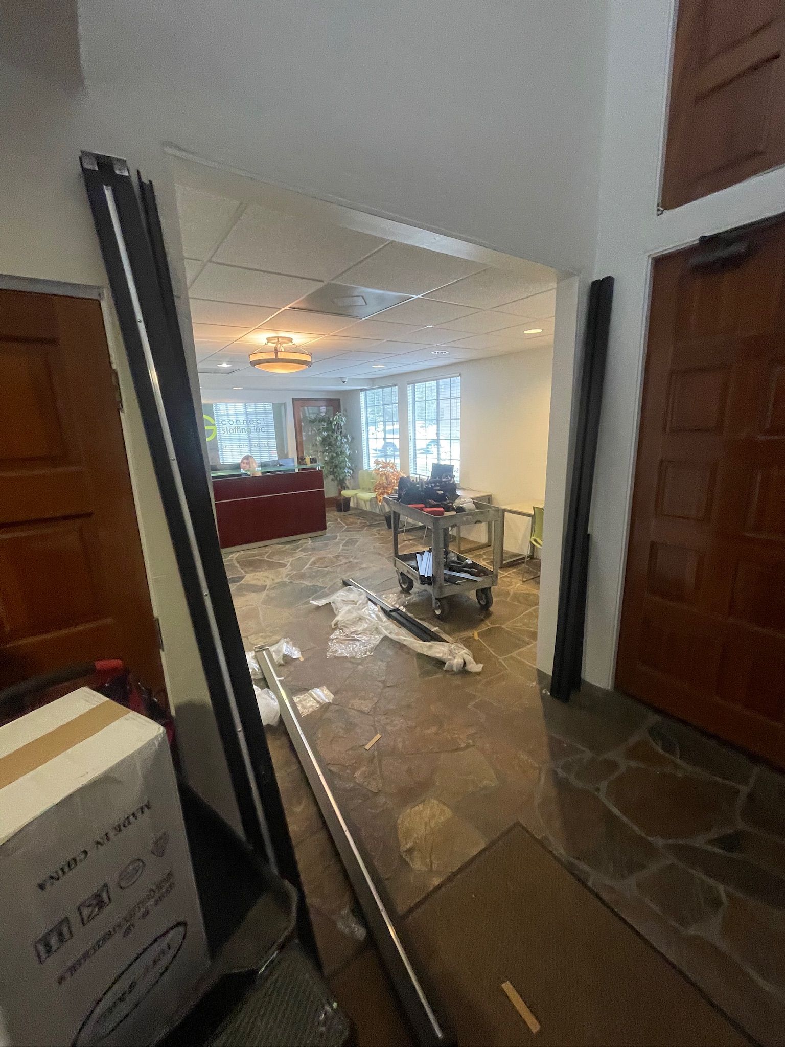 Interior hallway with exposed flooring, boxes, and open door to room with furniture and window.