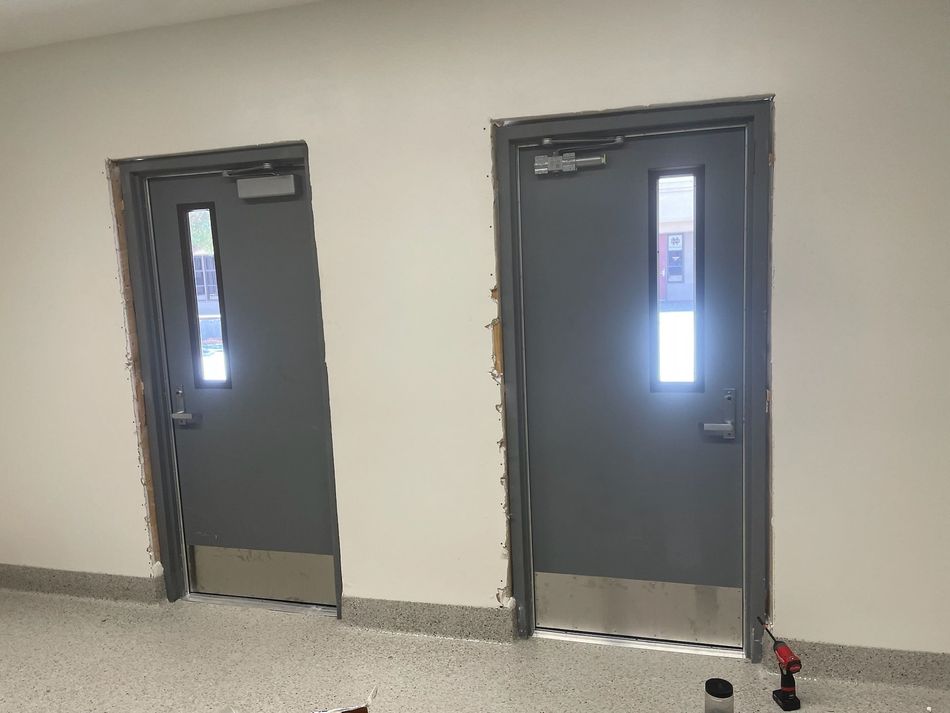 Loading docks on a warehouse exterior. Gray doors with black seals and yellow bumpers. Concrete and metal building.