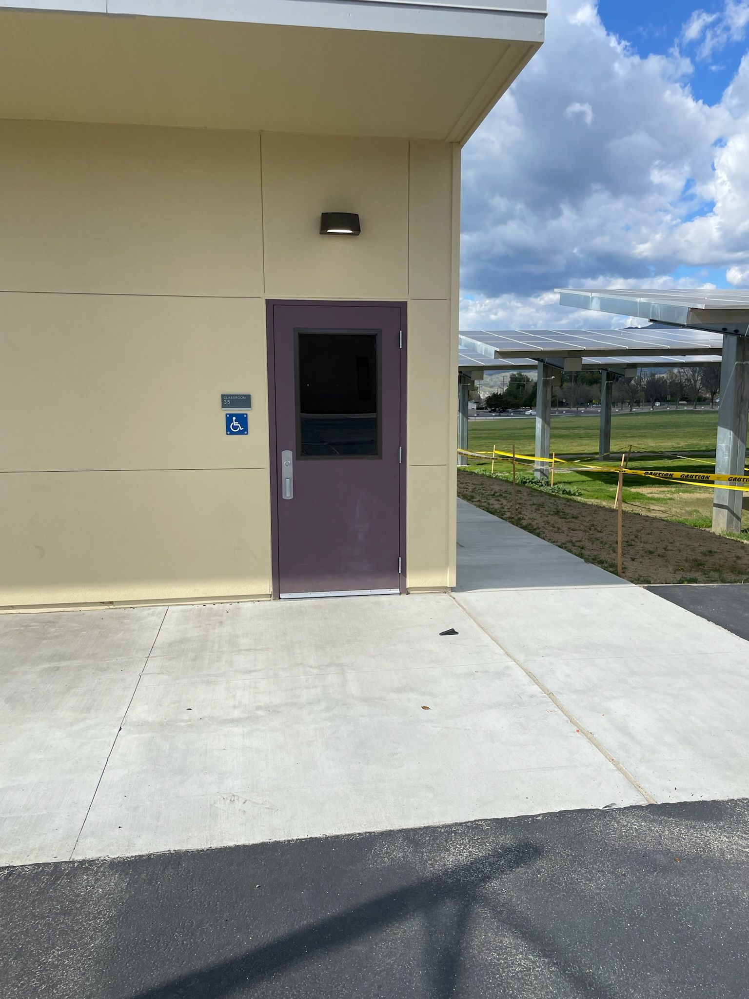 Tan building with purple door, accessible entrance sign. Concrete sidewalk, blue sky, and solar panels.