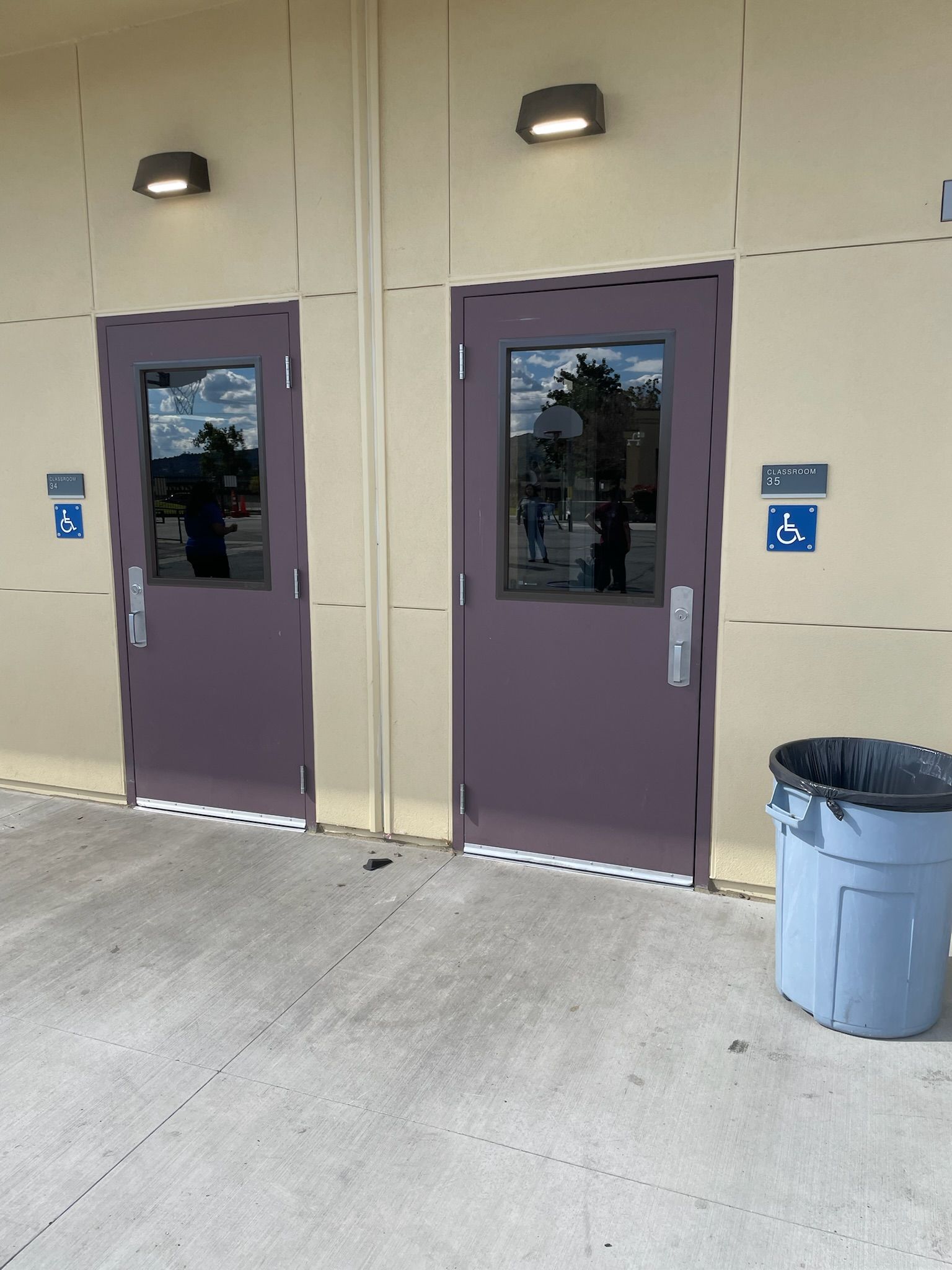 Two purple doors, bathroom entries, with glass panels and disability access symbols. Blue trash can nearby.