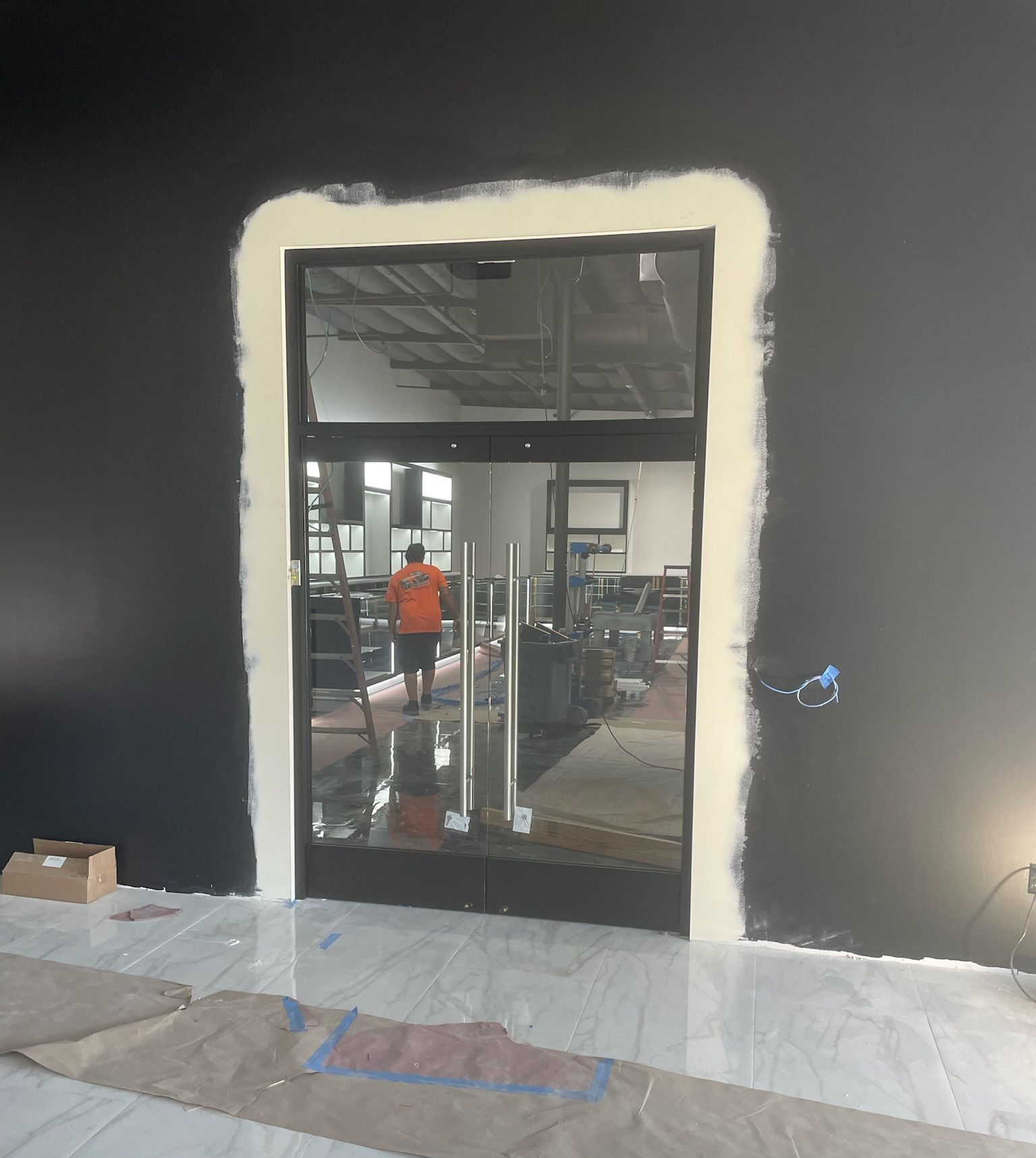 Glass door in a black-walled room. Cream-colored trim around the doorframe. Worker visible inside the room.