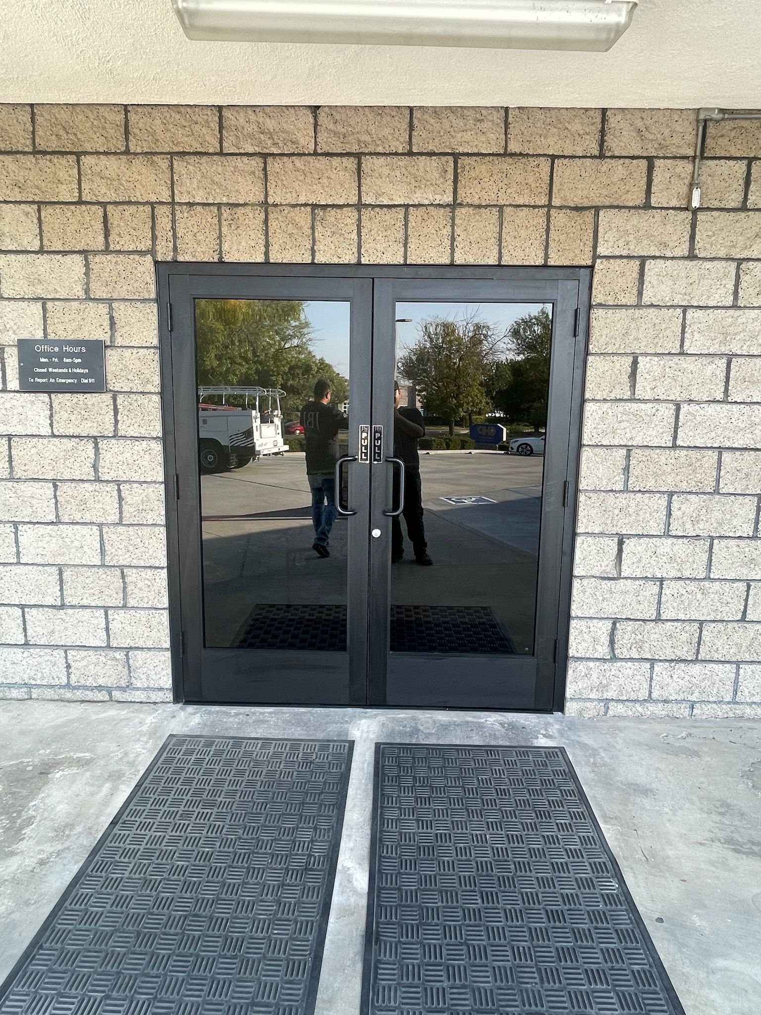 Double black doors with glass panels, brick wall, and two welcome mats.