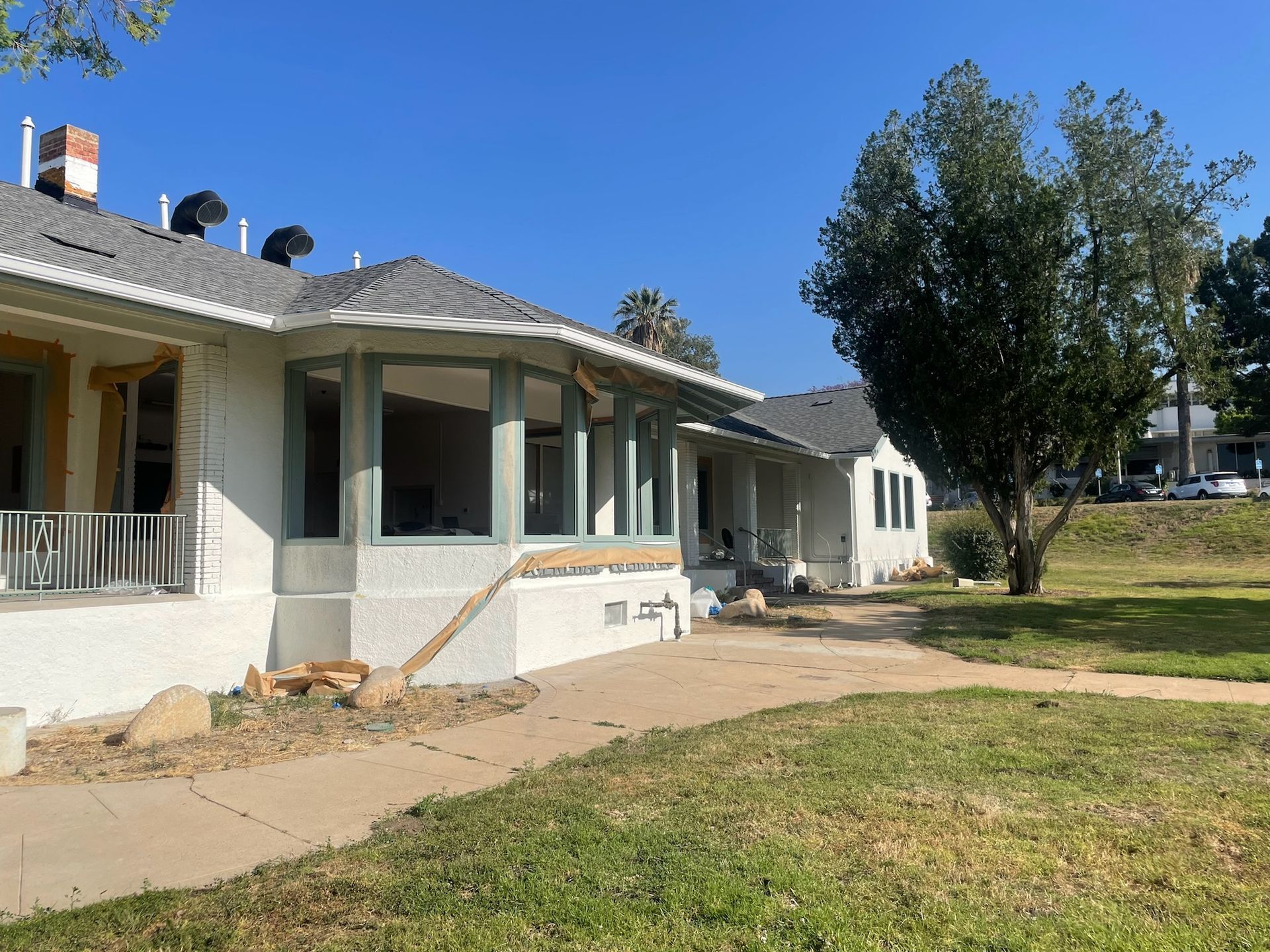 A white house under construction with a bay window and a cracked sidewalk.