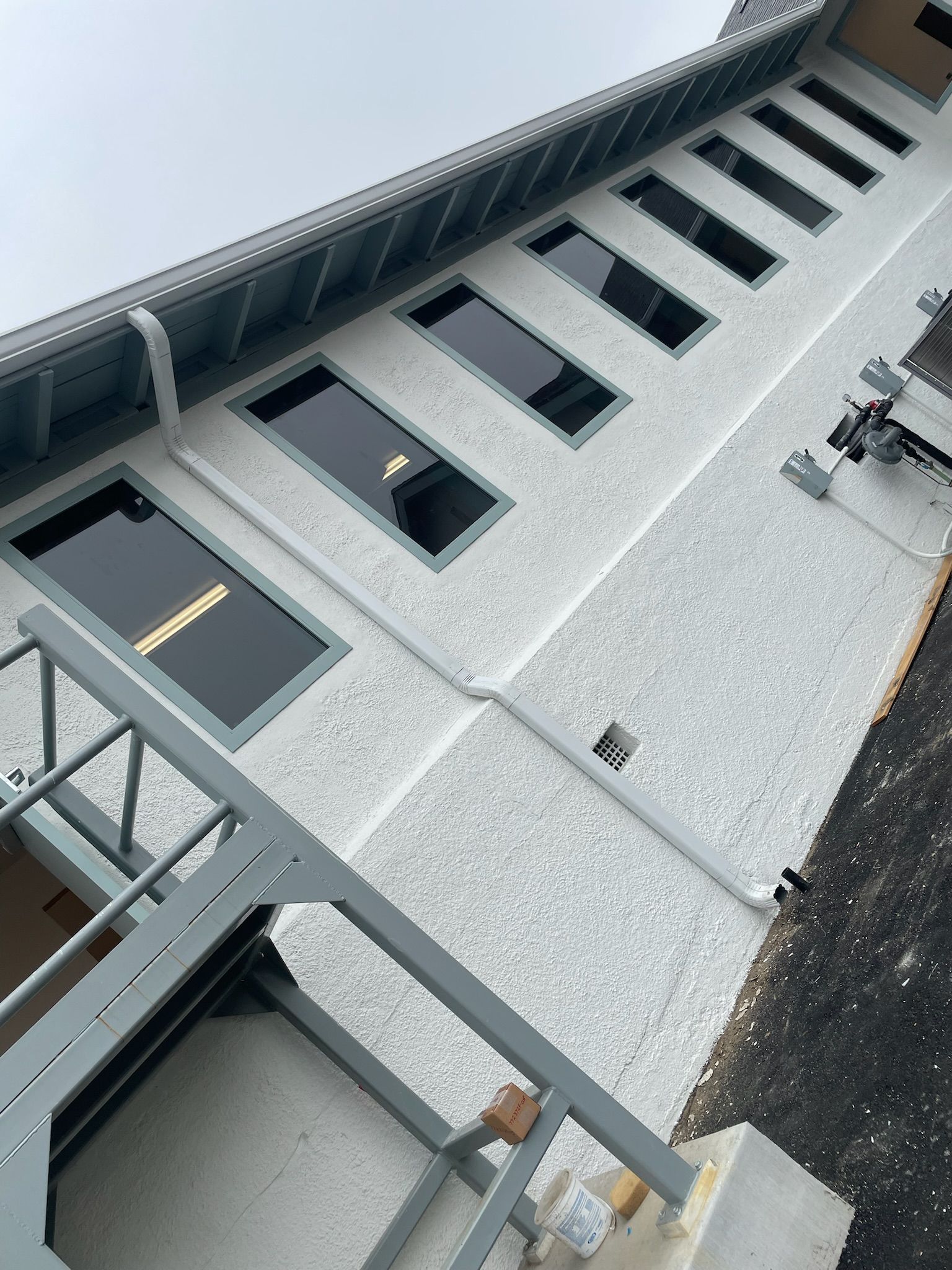 Exterior of a building with multiple rectangular windows, gray trim, and textured white stucco walls.