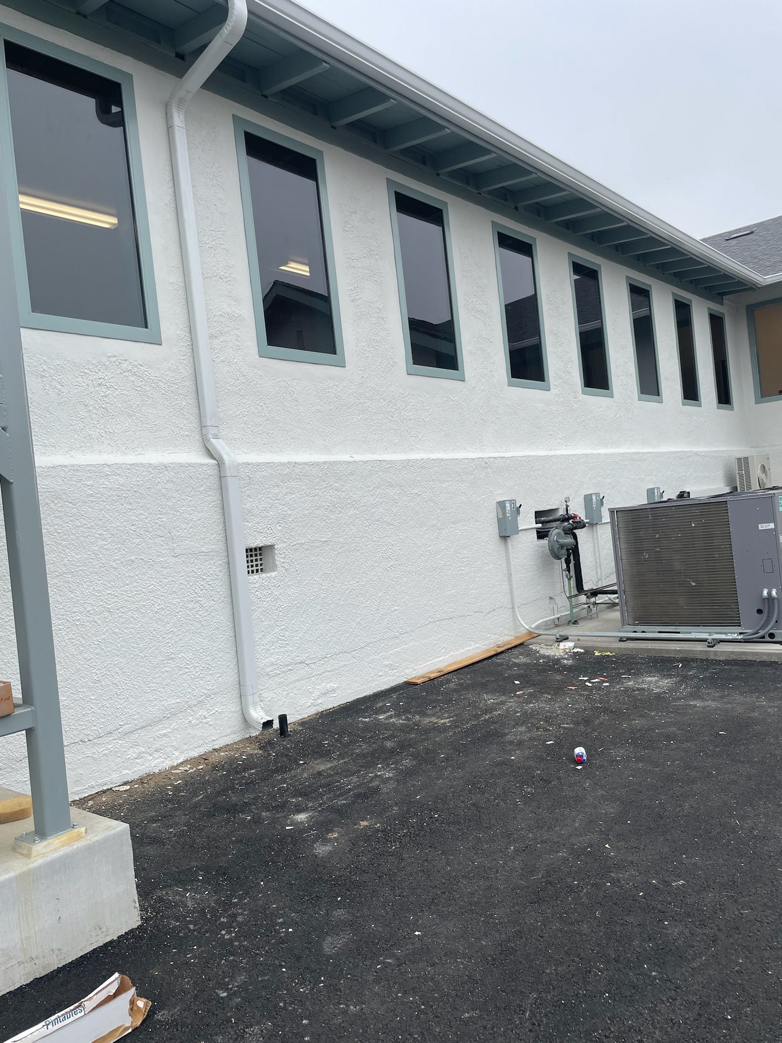 Exterior view of a white stucco building with multiple rectangular windows; dark roofing and a black gravel ground.